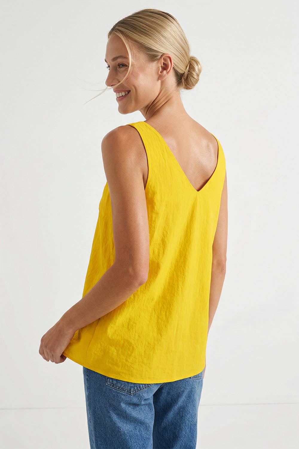 Woman wearing a golden yellow V-neck tank top with twisted cord straps and a sculptural flower detail at the shoulder.