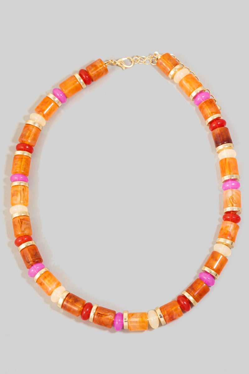 Short beaded choker necklace with orange, coral, peach, and pink resin beads and gold-tone spacers on a white necklace display.