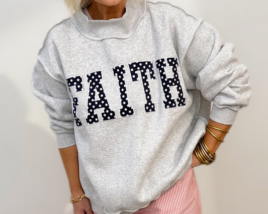 Heather gray oversized mock-neck sweatshirt featuring bold navy polka-dot "FAITH" embroidered lettering on the front