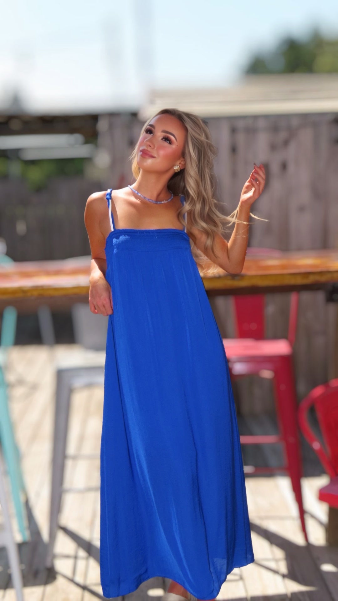 Woman wearing a flowing royal blue maxi dress with a smocked bust, thin cord straps and a relaxed silhouette.