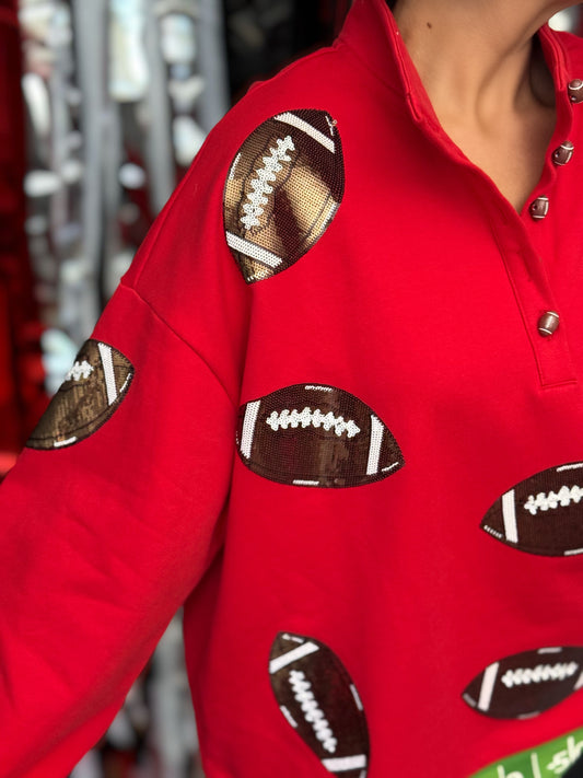 A close-up of a person wearing a bright red long-sleeve top with football-shaped appliques in brown, white, and black across the chest and sleeves.