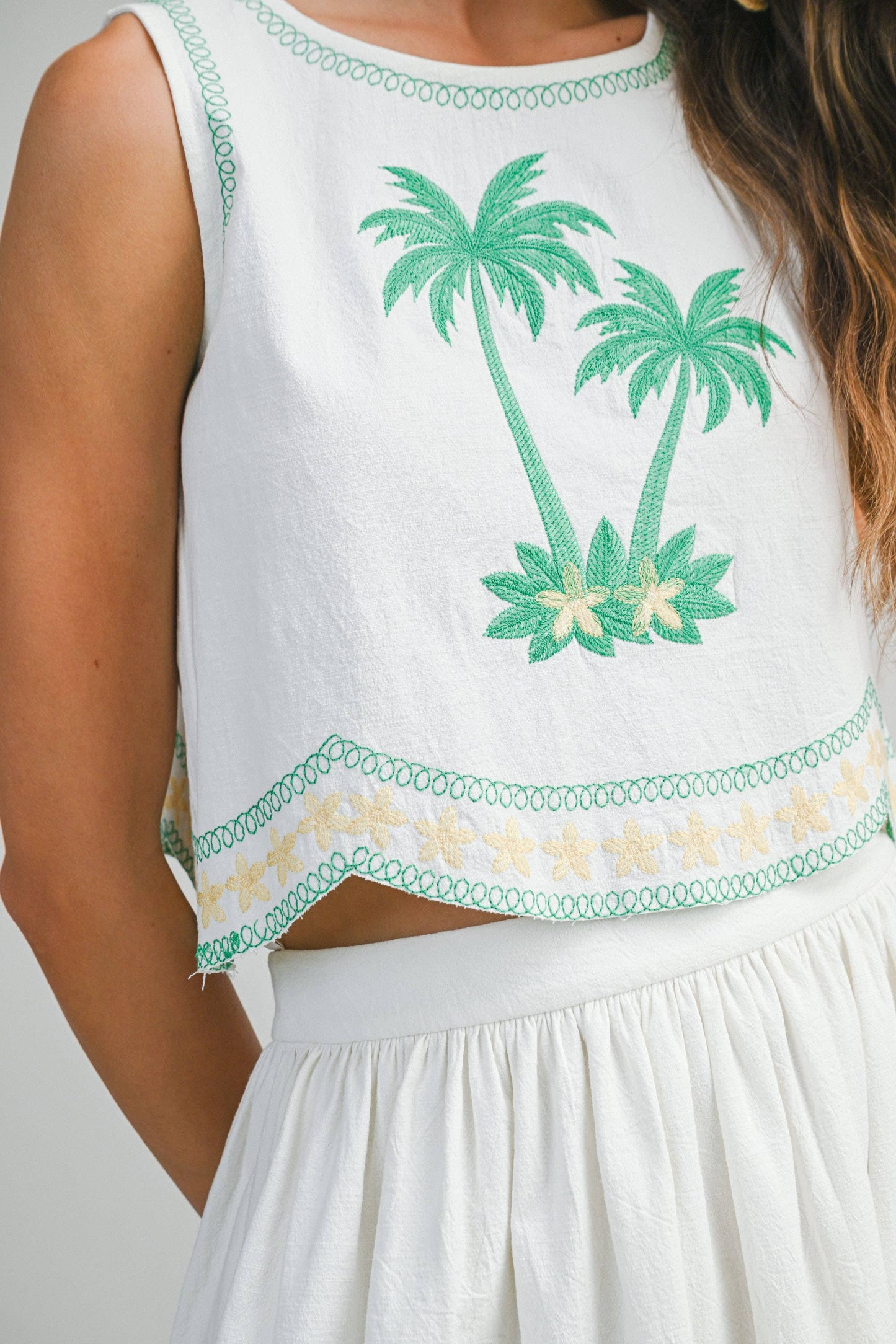 White sleeveless top with green palm tree embroidery on a plain background