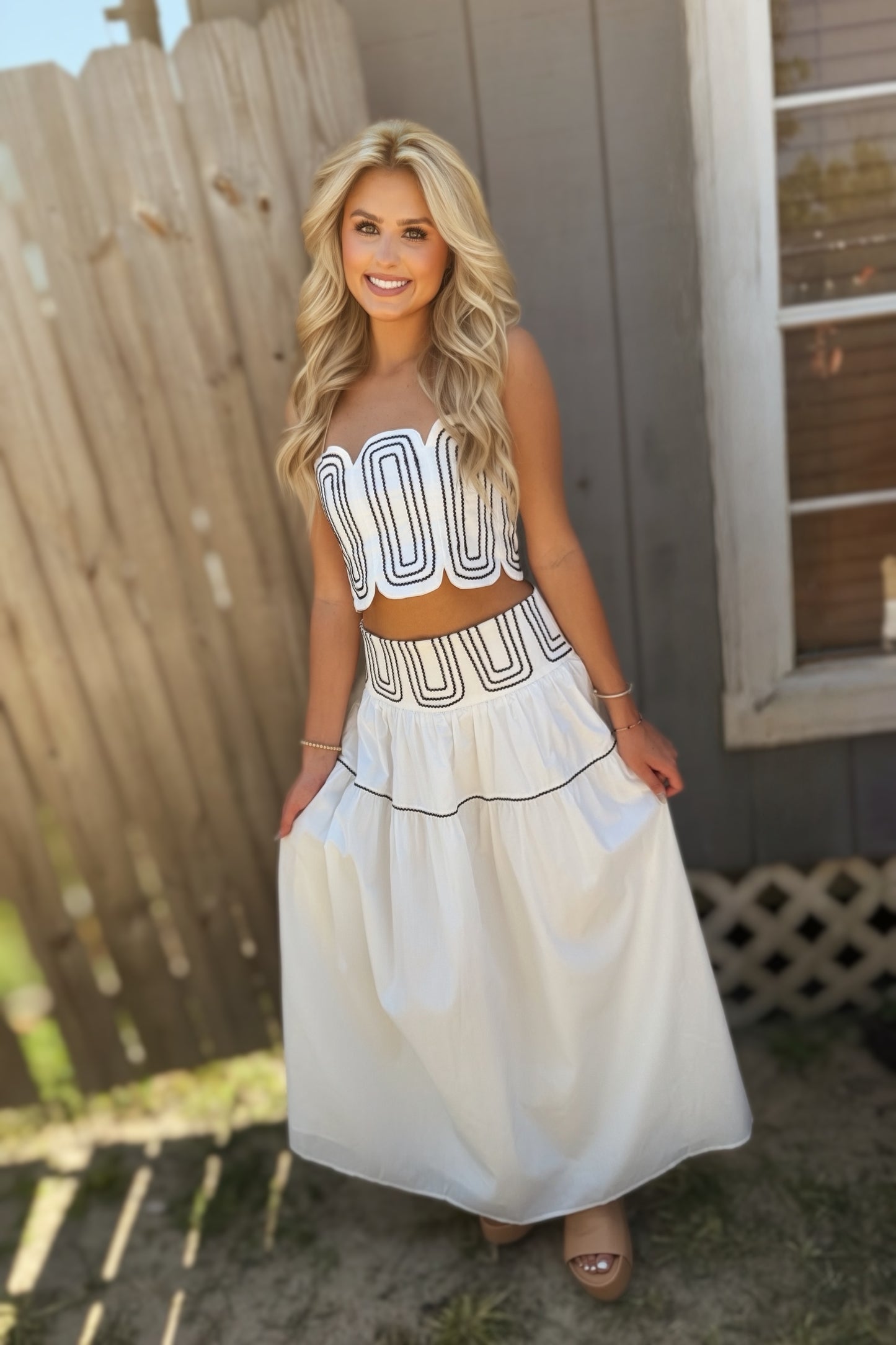 Woman wearing a white and navy two-piece set with a scalloped strapless crop top and flowing navy-trimmed maxi skirt.