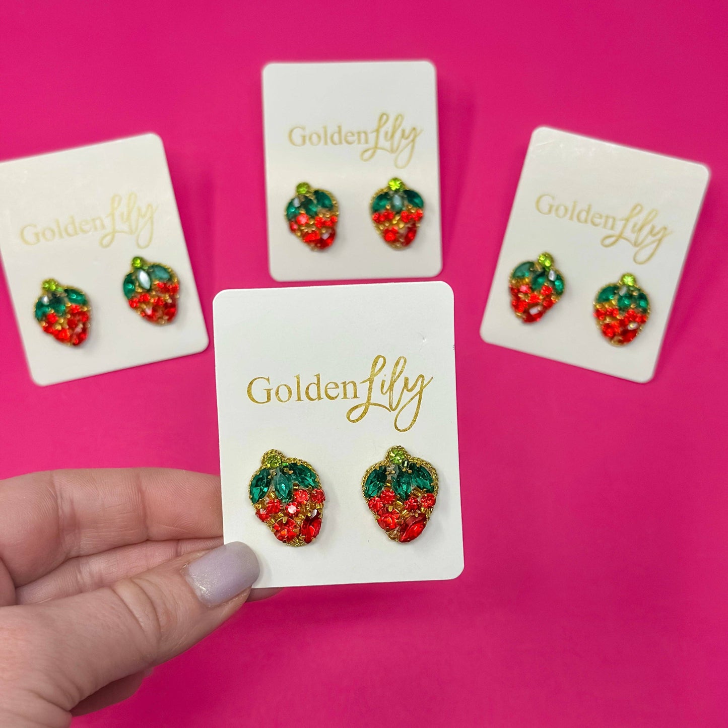 Red and green rhinestone strawberry statement earrings with crystal leaf accents and gold-tone trim displayed on jewelry cards.