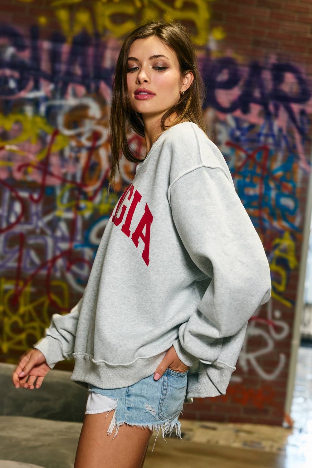 Woman wearing an oversized heather grey split-neck sweatshirt with large red Georgia lettering and drop shoulders.