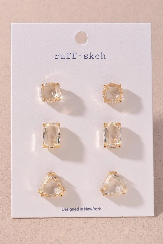 Three pairs of clear faceted glass stud earrings in round, rectangular, and rounded triangular shapes with gold-tone settings.

