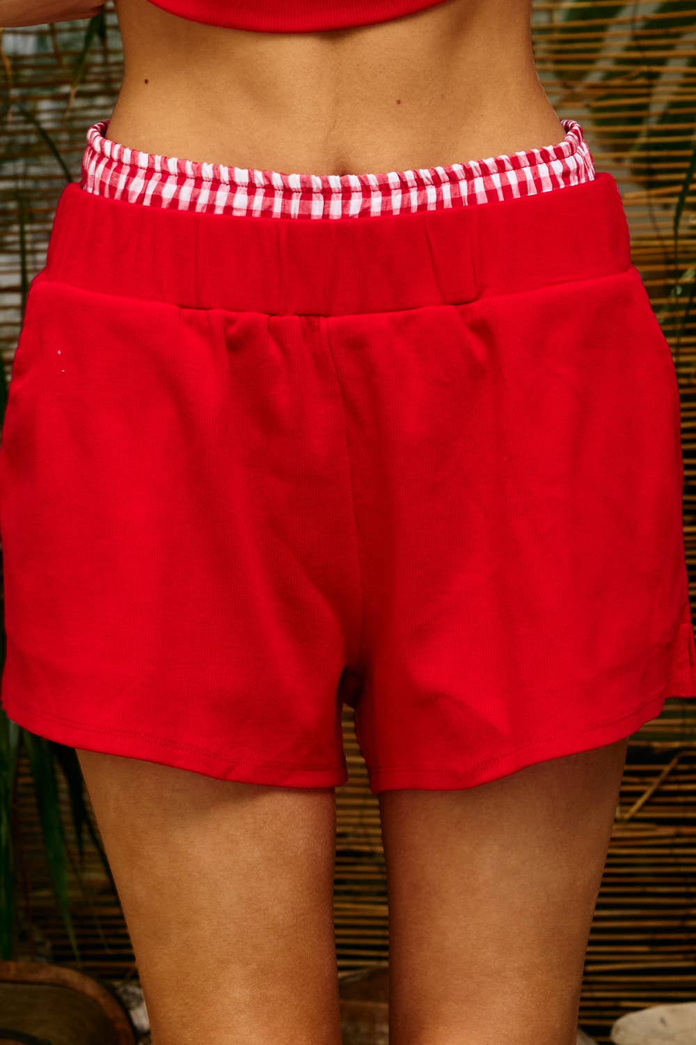 Woman wearing red ribbed lounge shorts with a red-and-white gingham contrast waistband and a relaxed wide-leg fit.