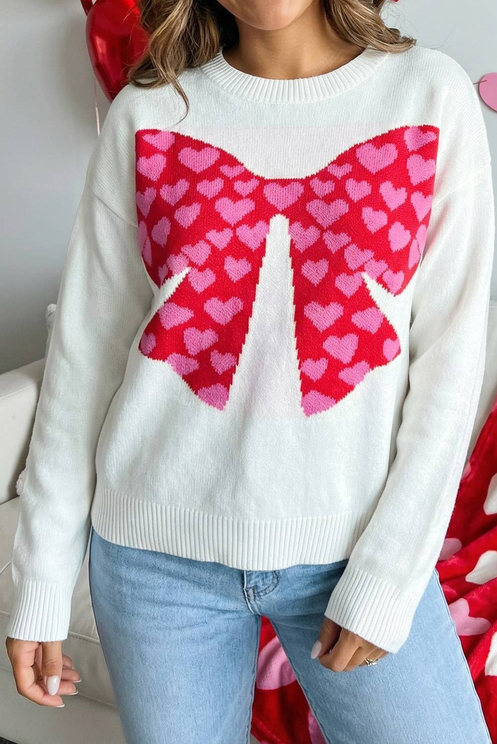 White sweater with a large pink heart bow design worn by a person.
