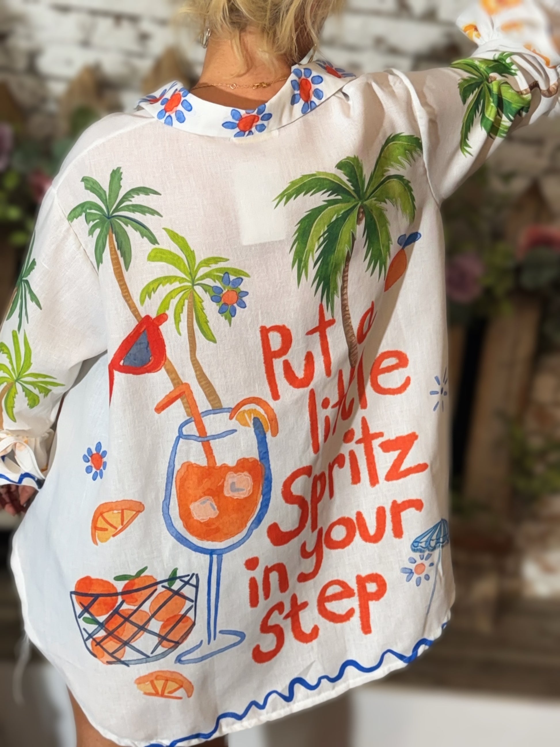 White Italian button-down resort shirt featuring colorful palm trees, citrus artwork, blueberries, and "Put a Little Spritz in Your Step" graphic.