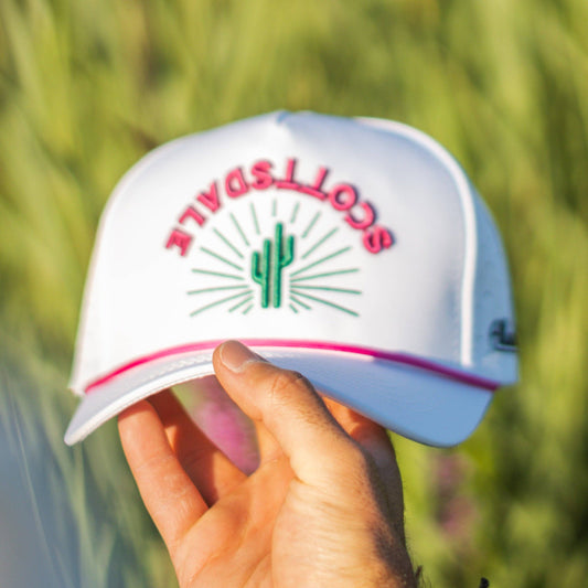 White cap with red text and green cactus design held by a hand against a blurred green background