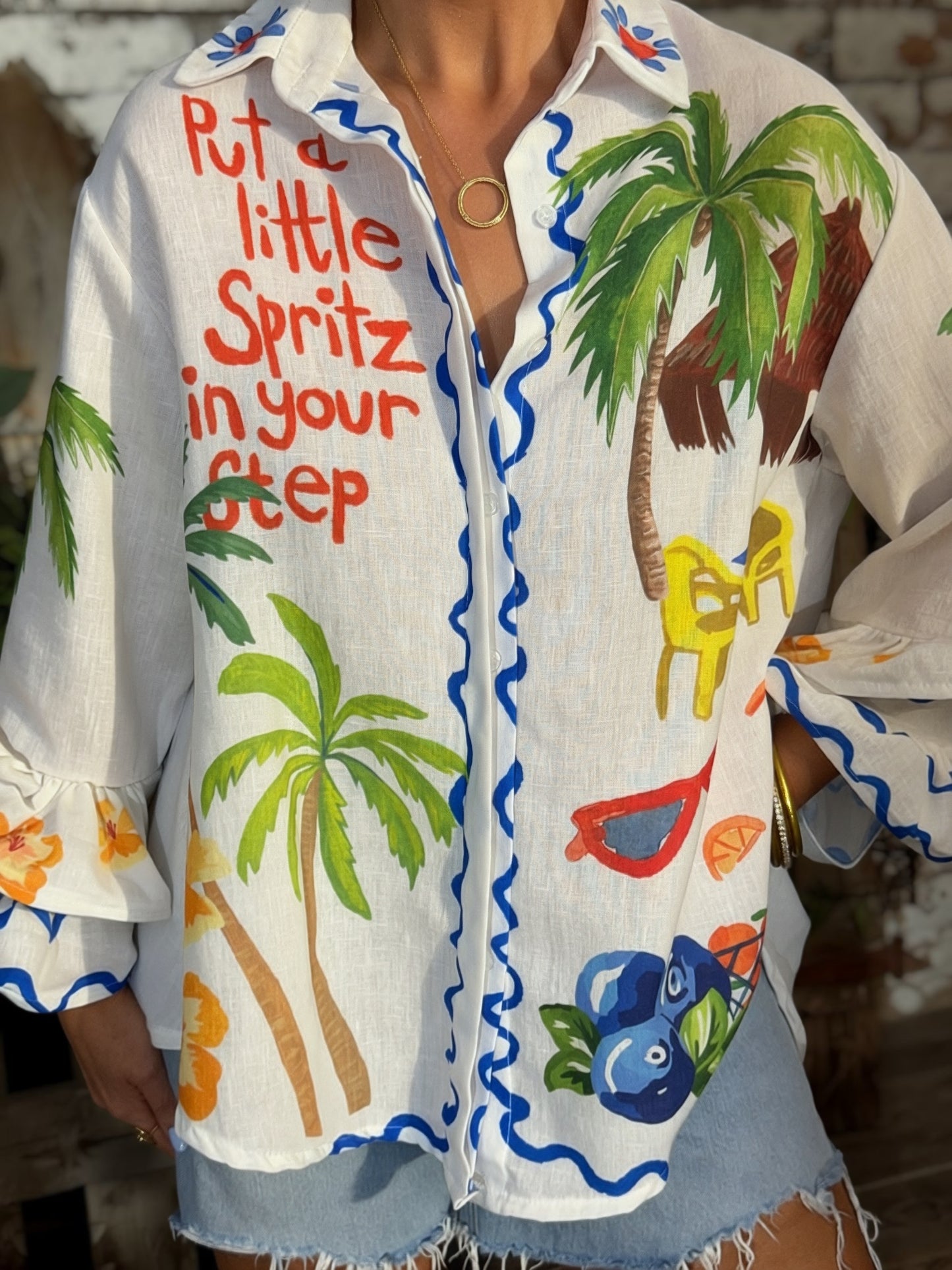 White Italian button-down resort shirt featuring colorful palm trees, citrus artwork, blueberries, and "Put a Little Spritz in Your Step" graphic.