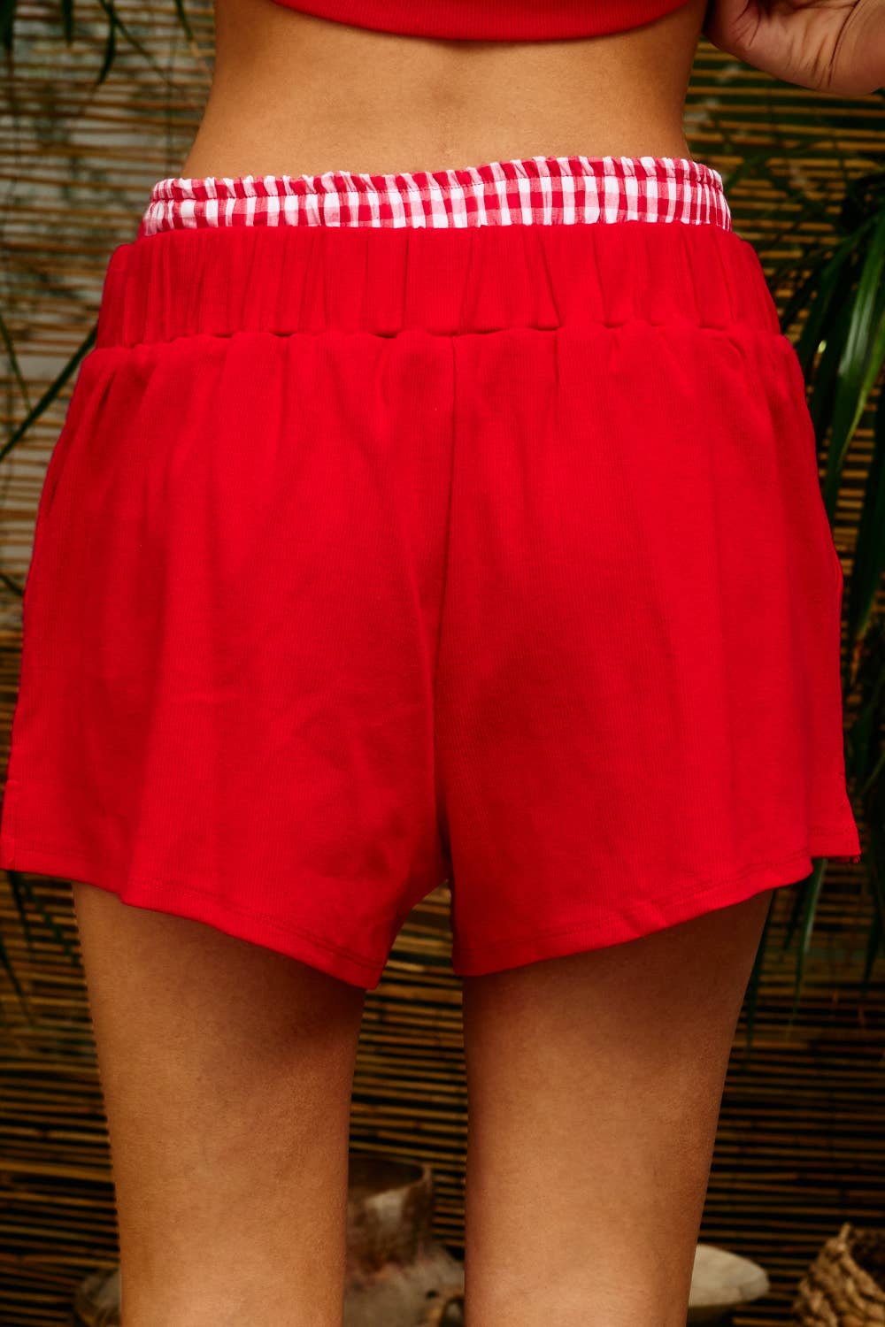 Woman wearing red ribbed lounge shorts with a red-and-white gingham contrast waistband and a relaxed wide-leg fit.