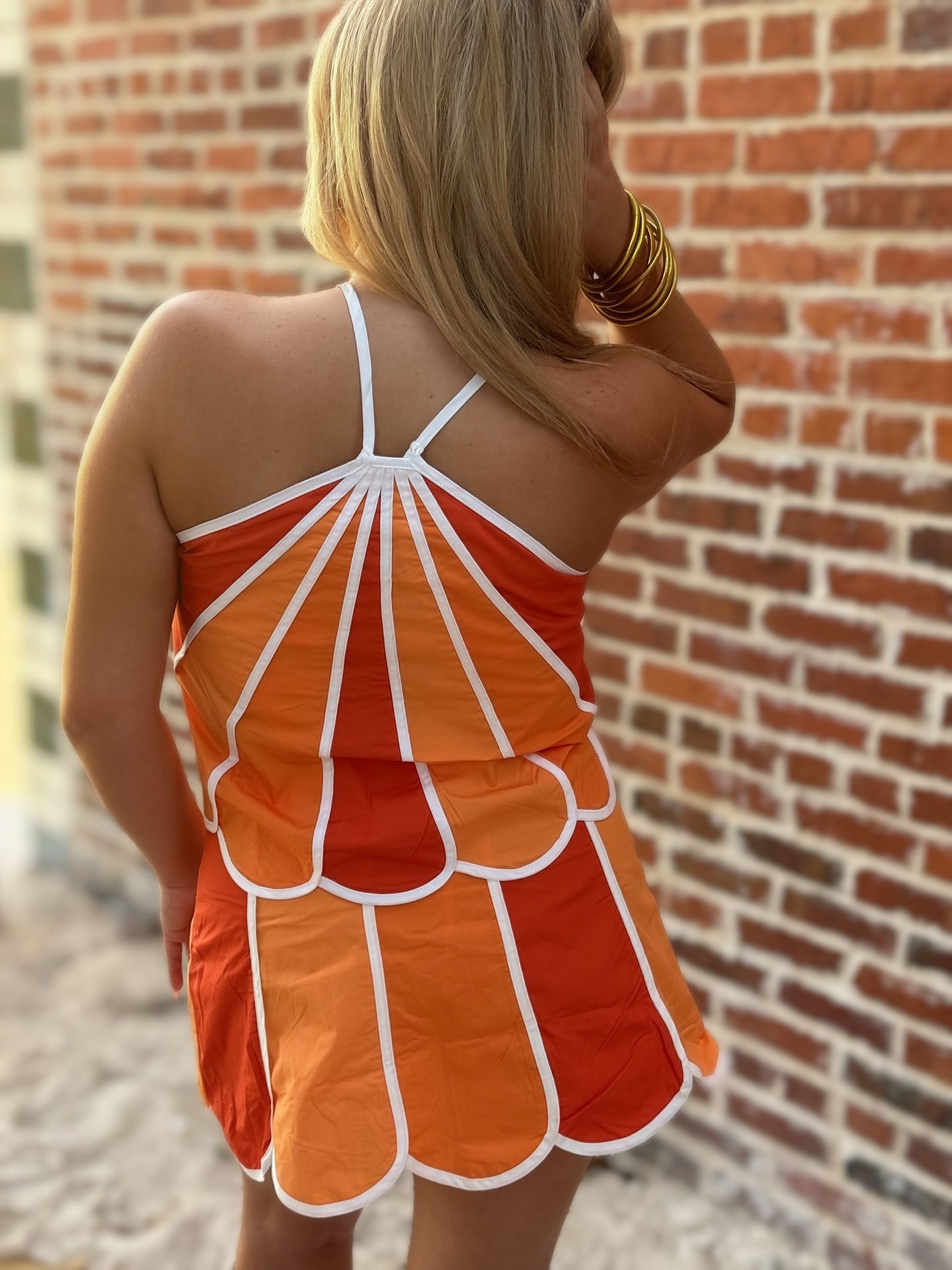 Woman wearing an orange and red colorblock two-piece set featuring a gathered halter top and high-rise scalloped mini skirt with white contrast piping.