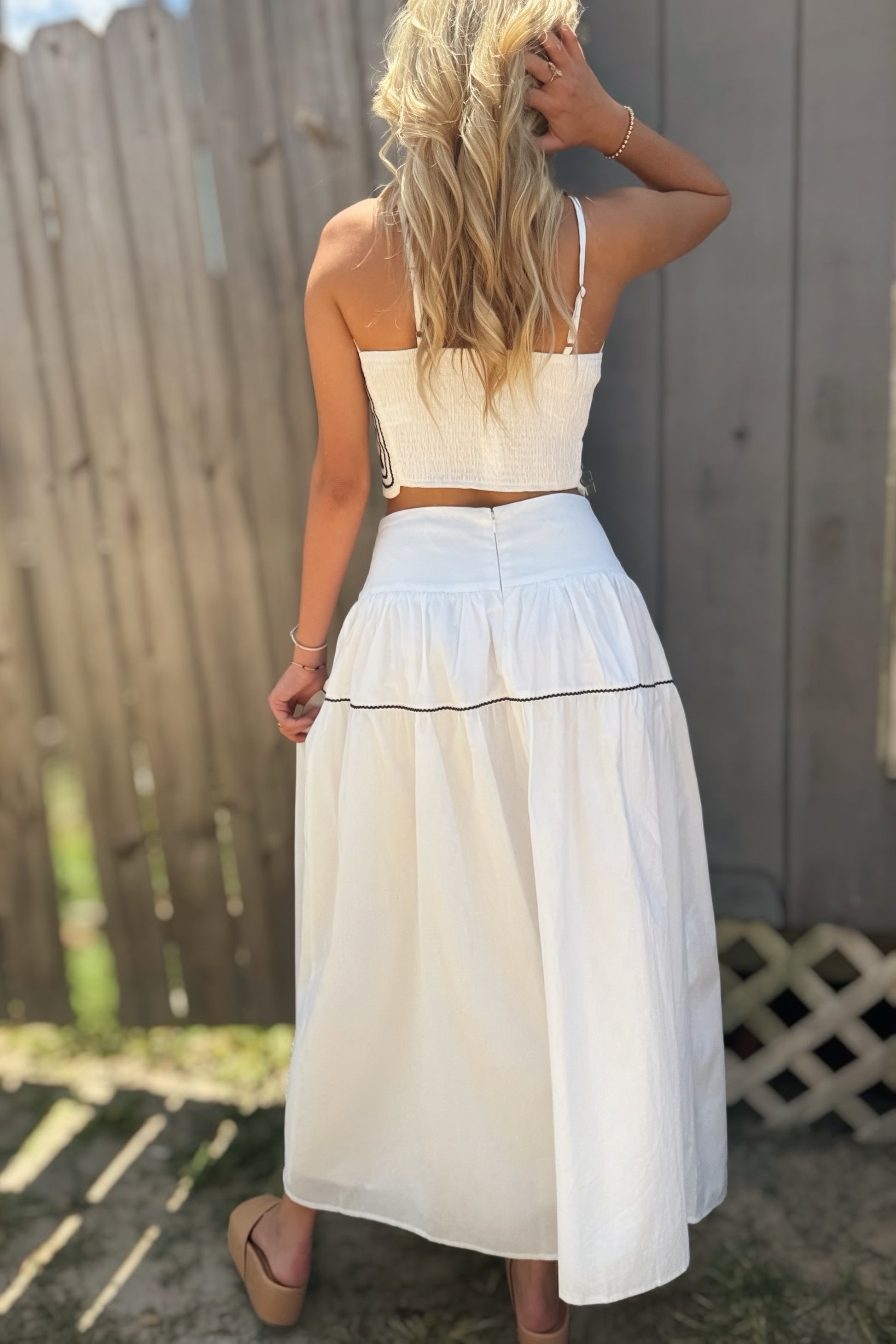 Woman wearing a white and navy two-piece set with a scalloped strapless crop top and flowing navy-trimmed maxi skirt.