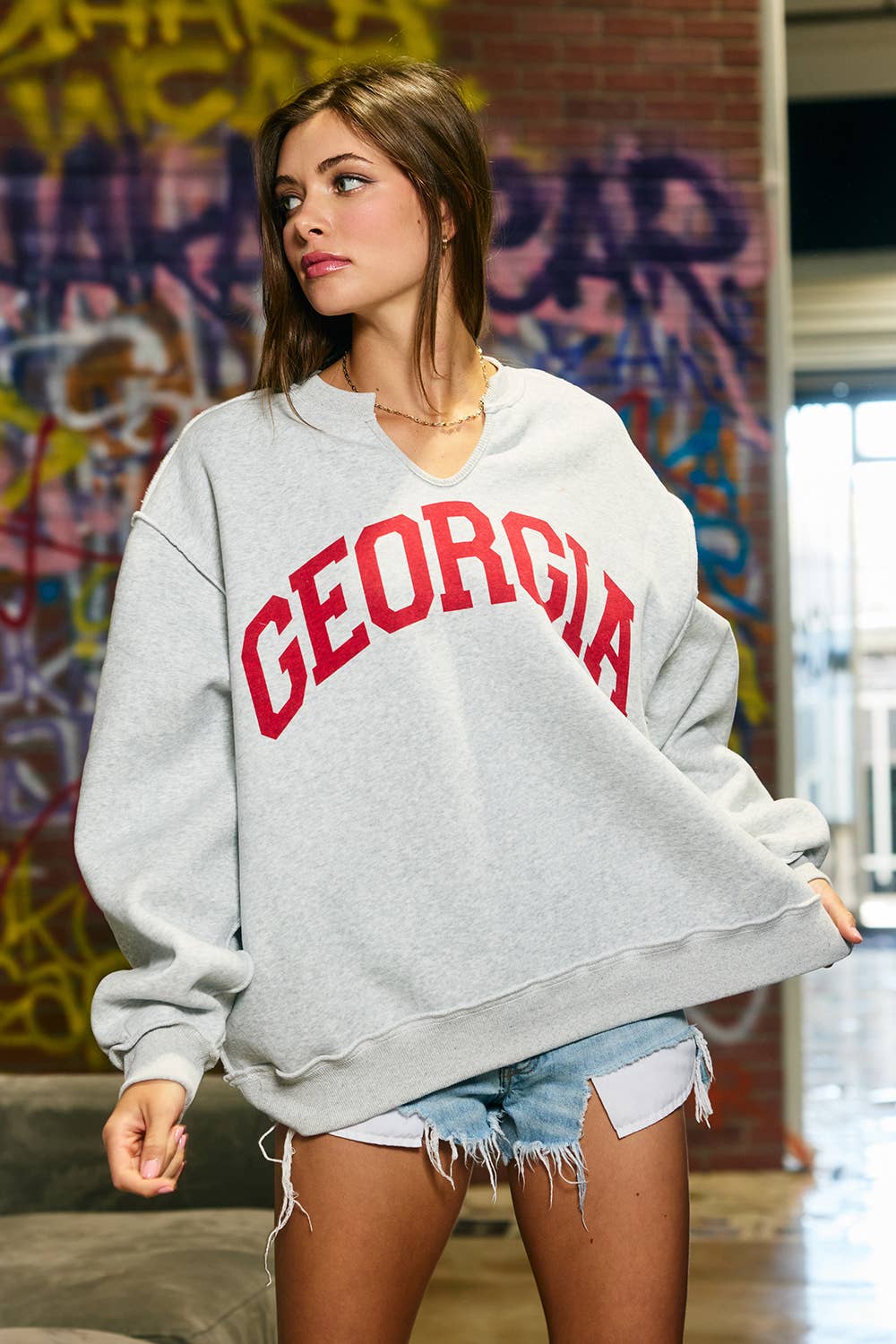Woman wearing an oversized heather grey split-neck sweatshirt with large red Georgia lettering, drop shoulders and a front pocket.