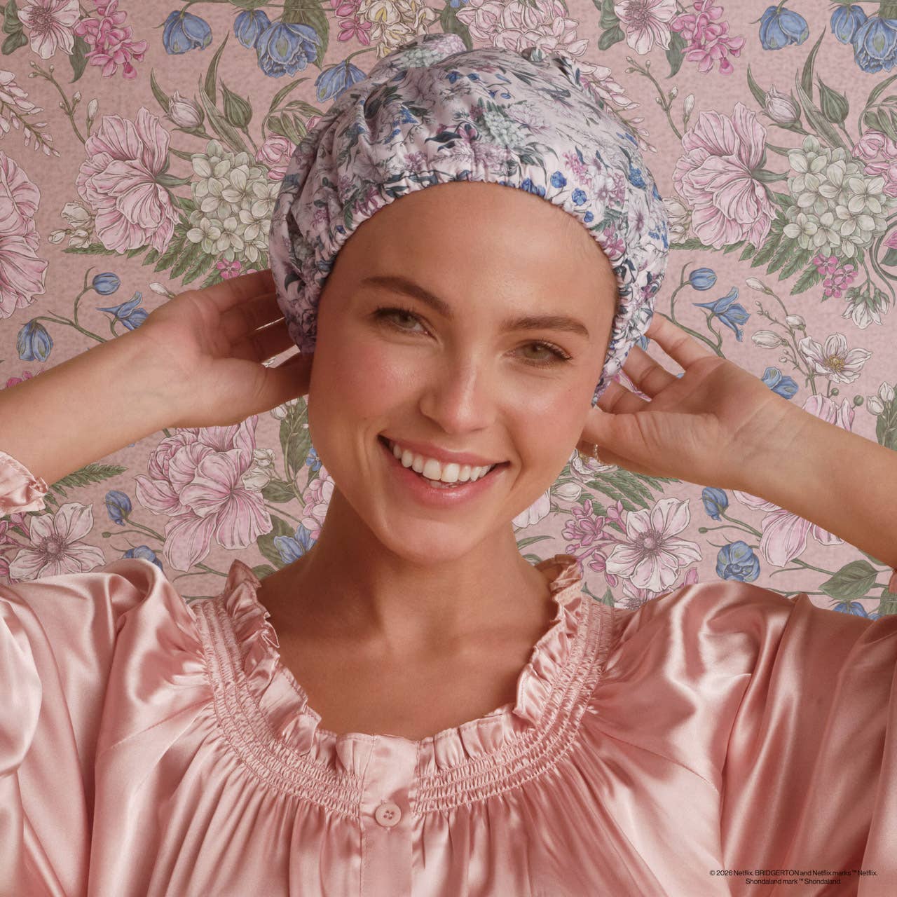 Woman wearing a floral satin headband and pink satin robe against a floral background