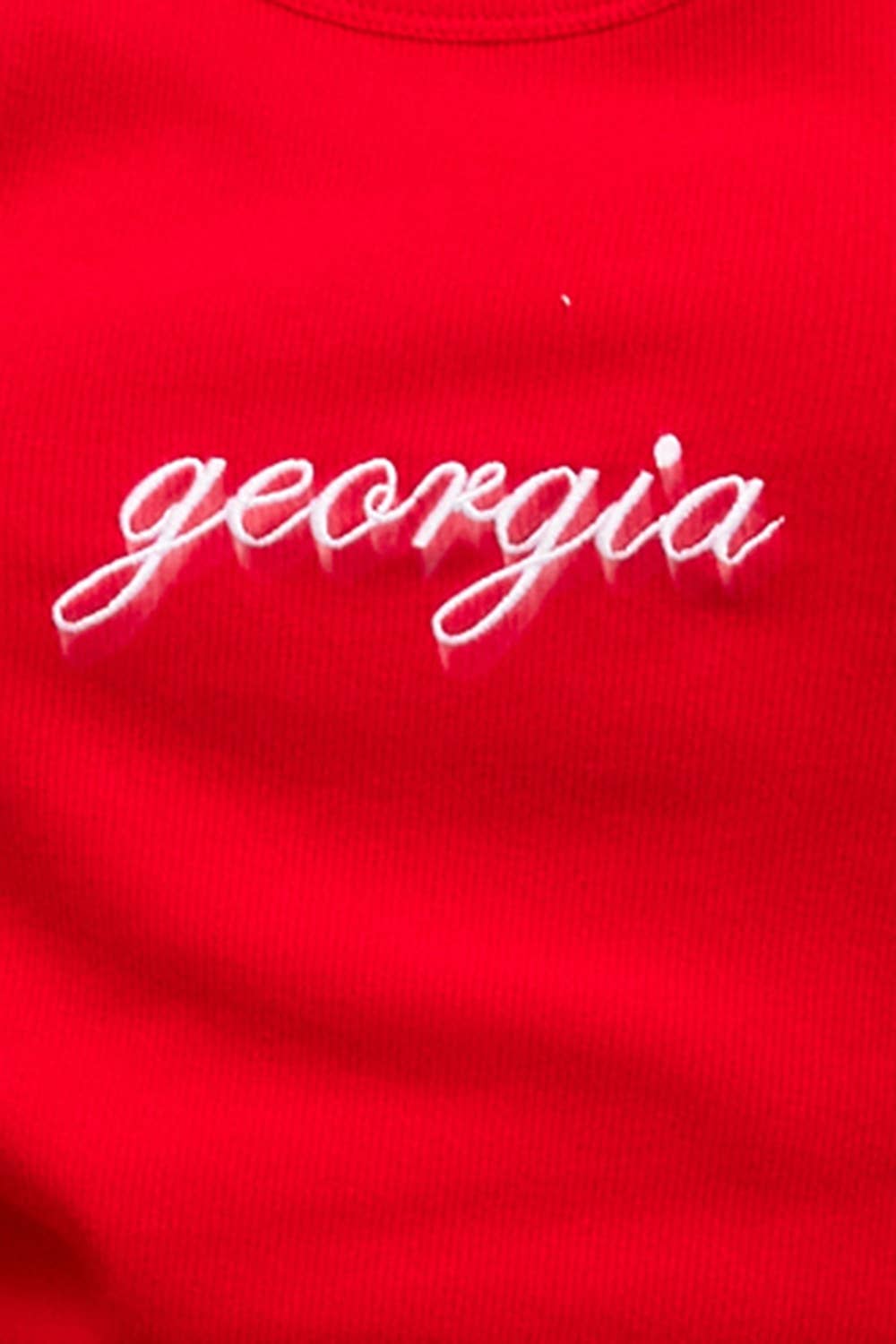 Woman wearing a fitted red ribbed tank top with white cursive “georgia” embroidery 