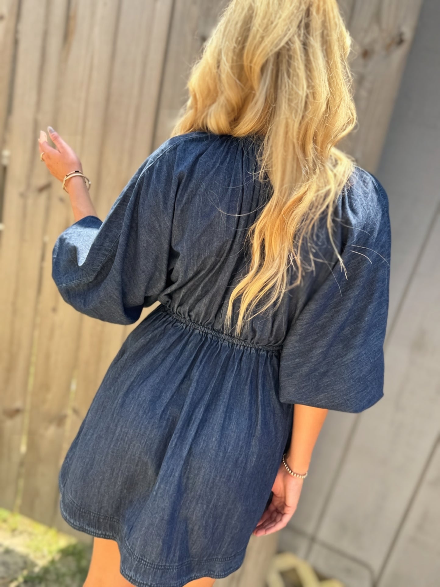 Woman wearing a dark wash denim mini dress with a deep V-neckline, three-quarter puff sleeves and a flared skirt.