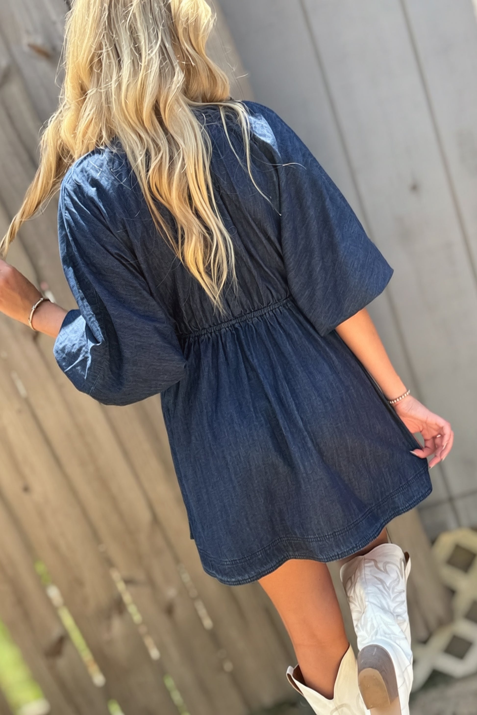 Woman wearing a dark wash denim mini dress with a deep V-neckline, three-quarter puff sleeves and a flared skirt.