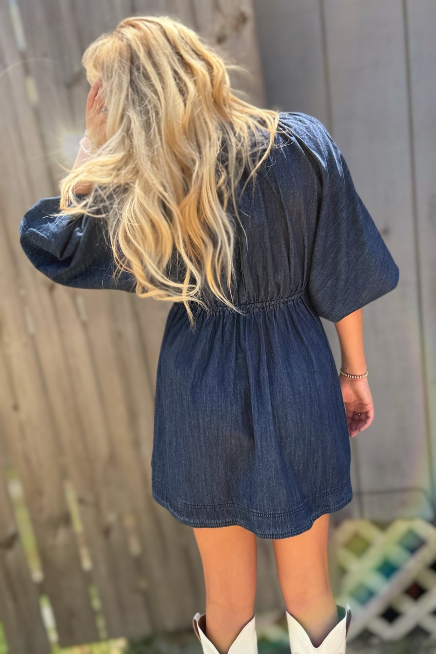 Woman wearing a dark wash denim mini dress with a deep V-neckline, three-quarter puff sleeves and a flared skirt.