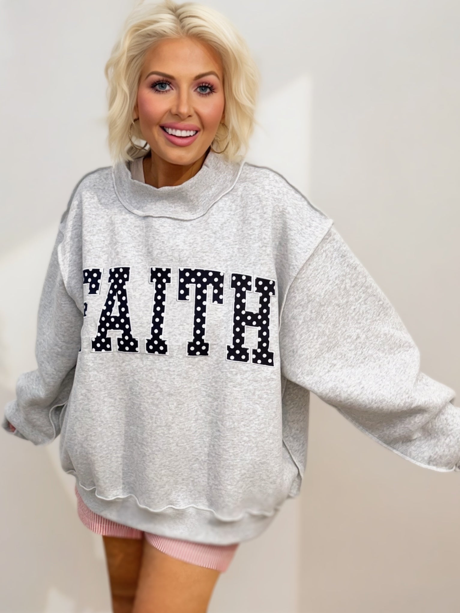 Heather gray oversized mock-neck sweatshirt featuring bold navy polka-dot "FAITH" embroidered lettering on the front