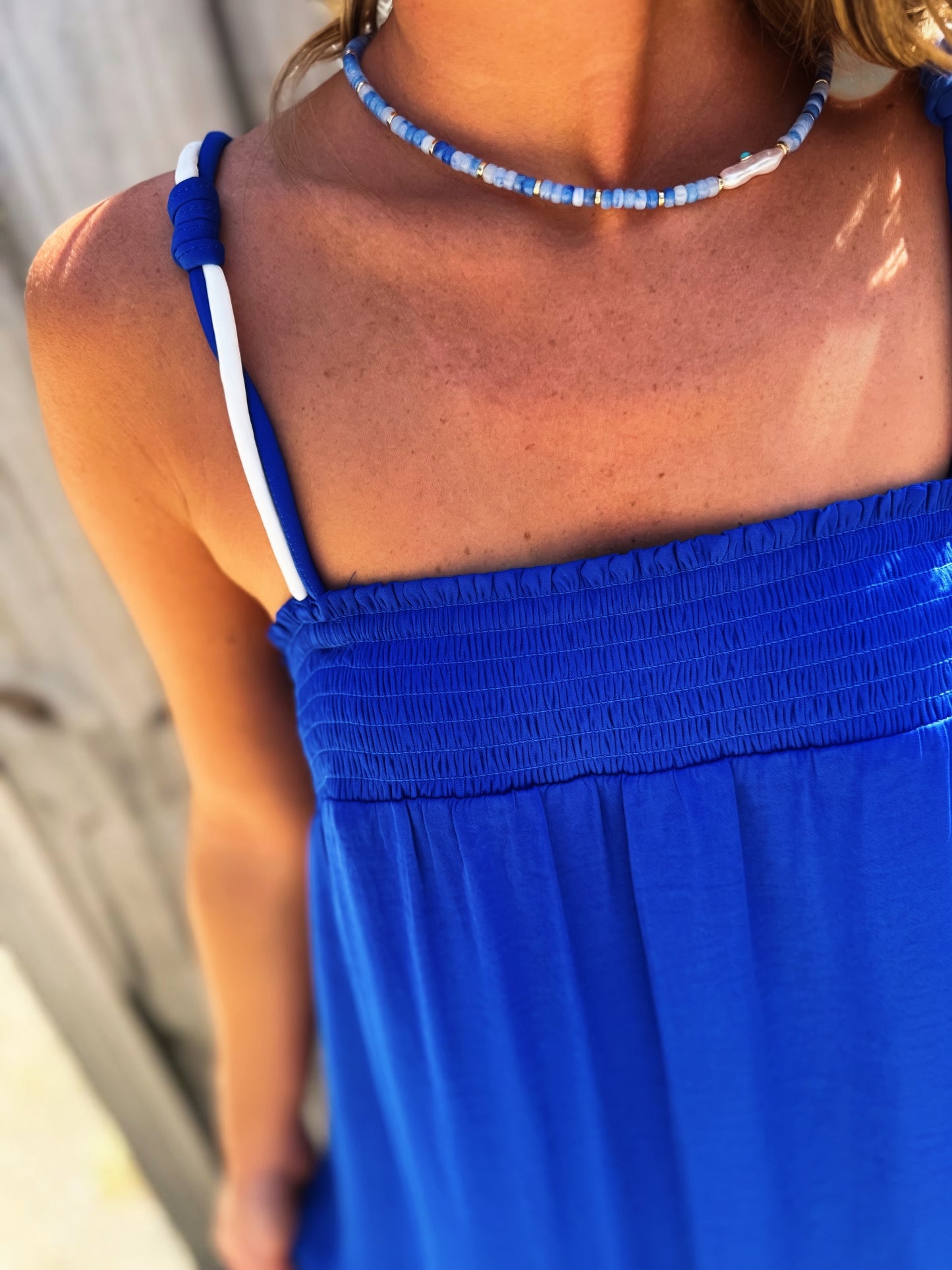 Woman wearing a flowing royal blue maxi dress with a smocked bust, thin cord straps and a relaxed silhouette.