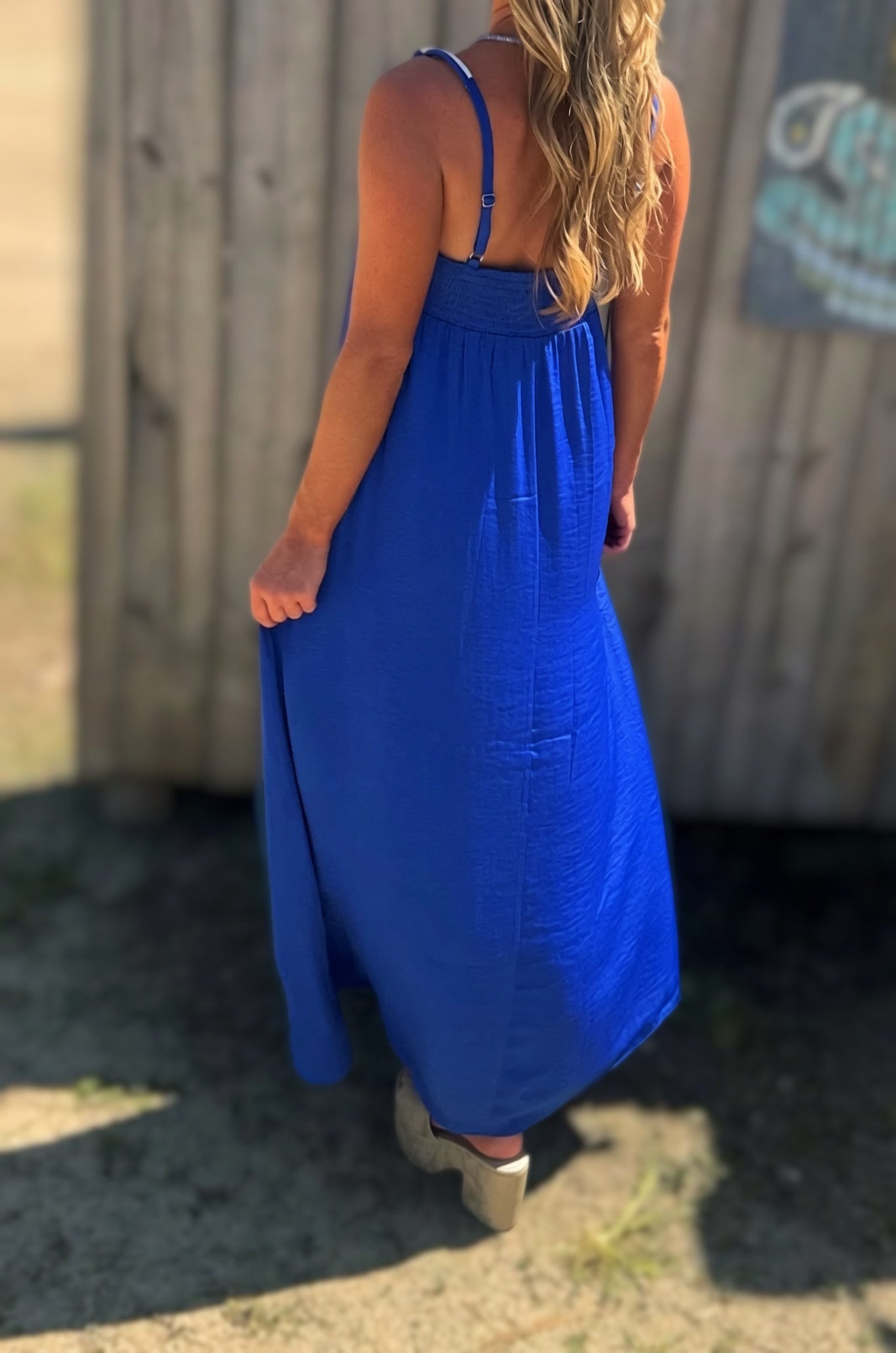 Woman wearing a flowing royal blue maxi dress with a smocked bust, thin cord straps and a relaxed silhouette.