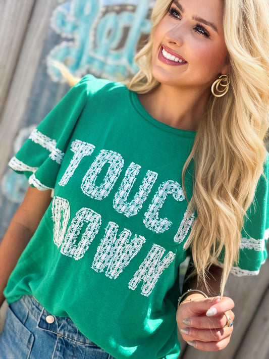 Woman wearing a green Touchdown game day top with white lace lettering and lace-trimmed bubble sleeves.