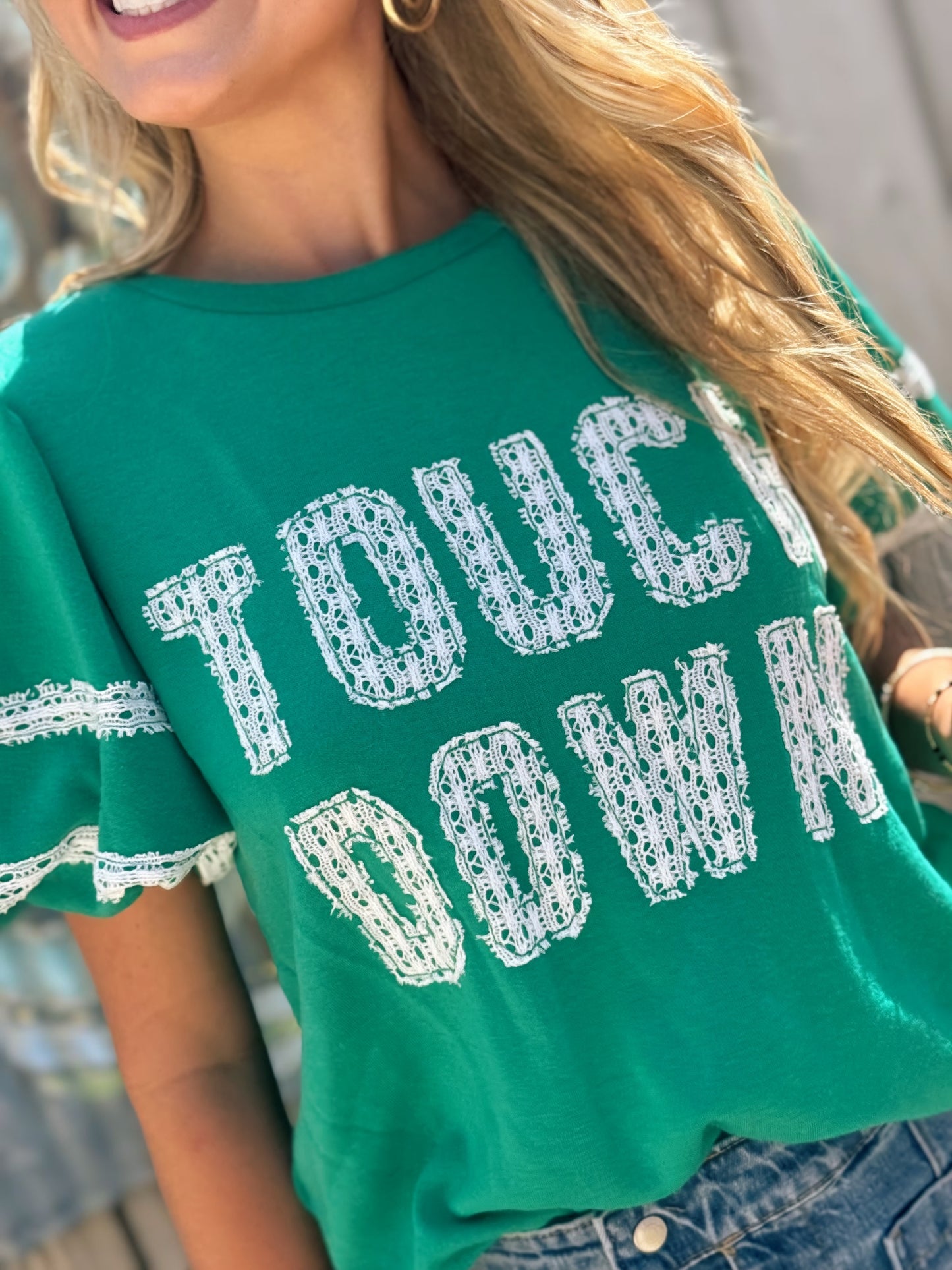 Woman wearing a green Touchdown game day top with white lace lettering and lace-trimmed bubble sleeves.