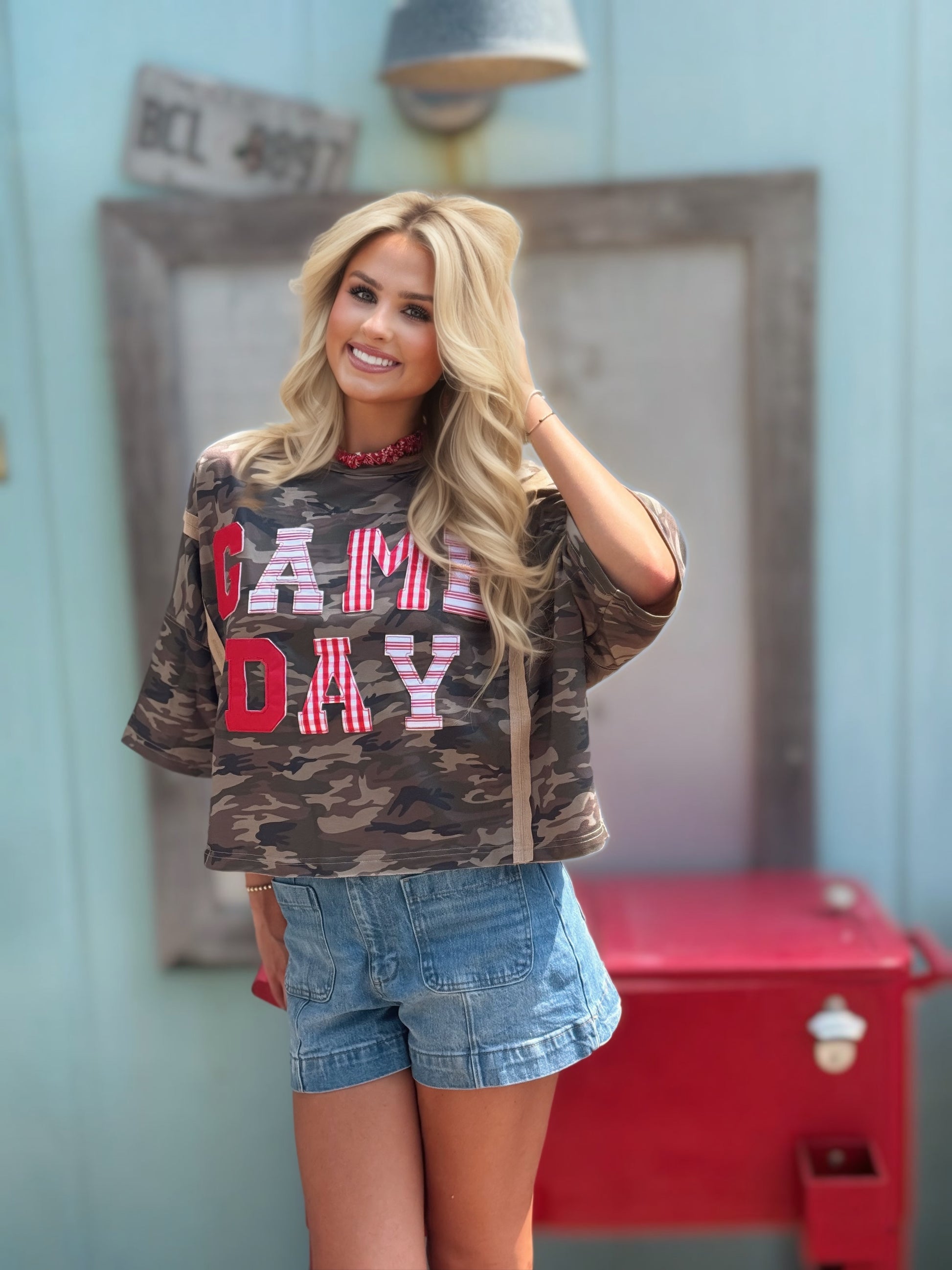 Woman wearing an oversized washed camouflage game day top with red, white and striped patchwork lettering.