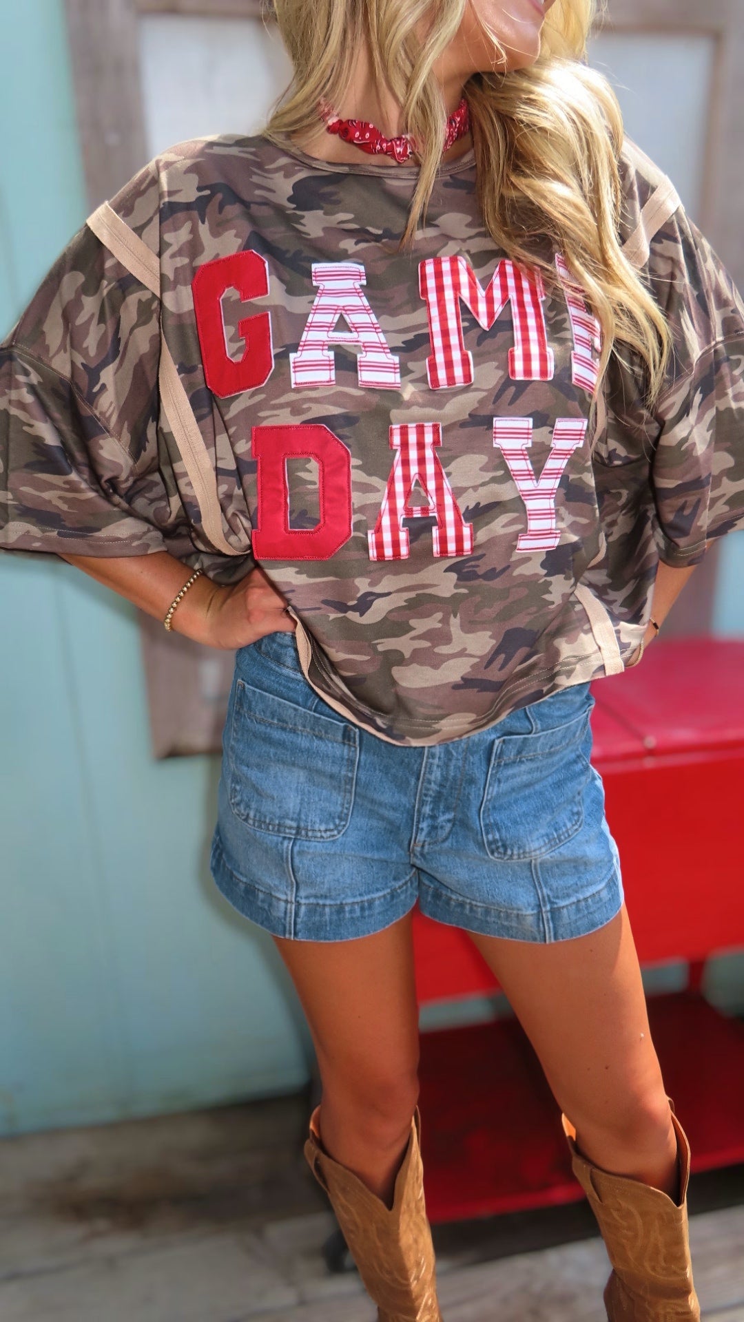 Woman wearing an oversized washed camouflage game day top with red, white and striped patchwork lettering.