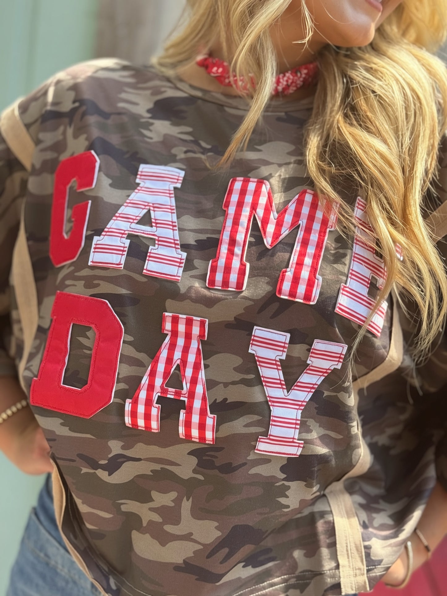 Woman wearing an oversized washed camouflage game day top with red, white and striped patchwork lettering.