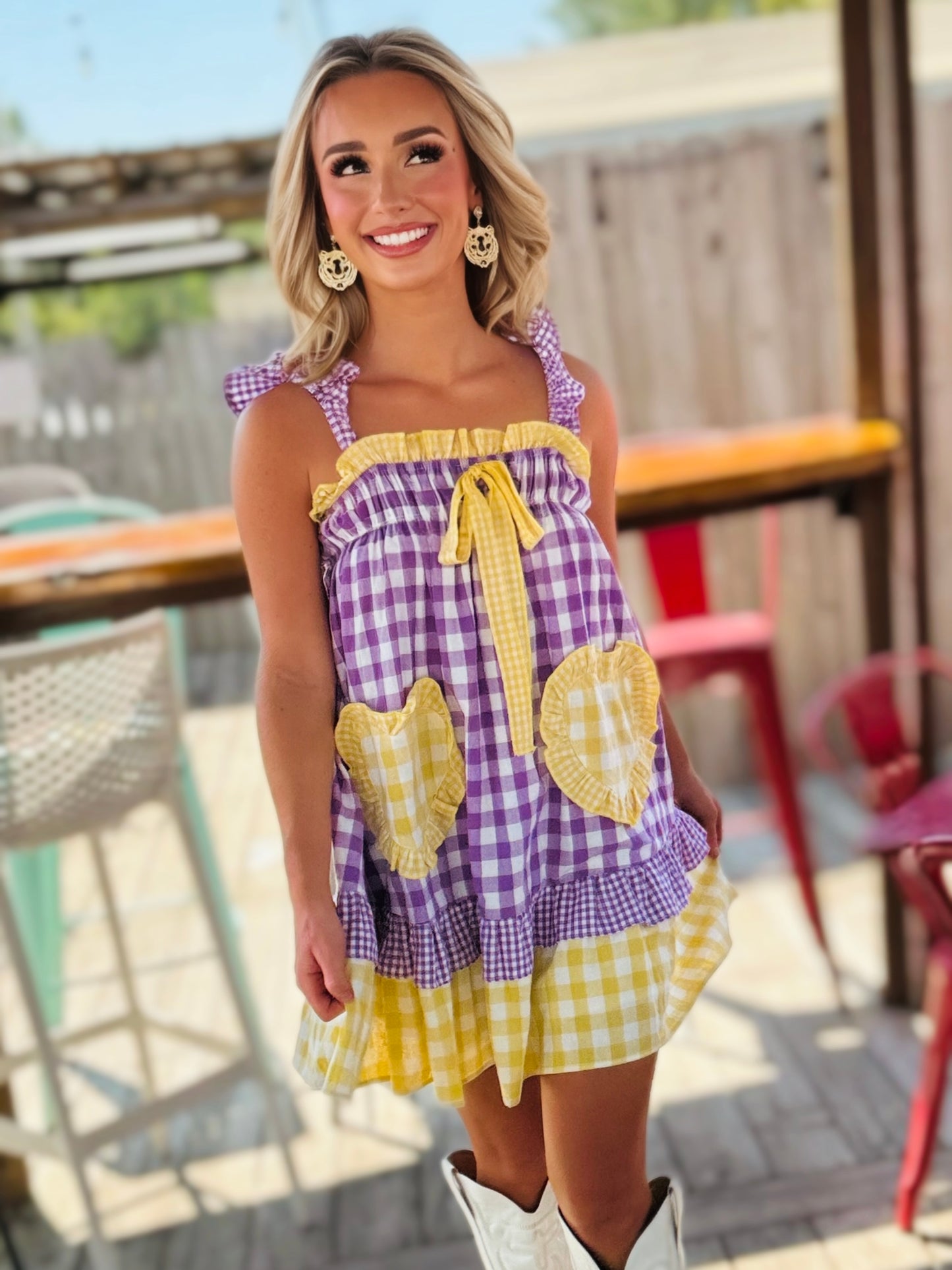 Woman wearing a purple and gold gingham babydoll mini dress with ruffle trim, a front tie and oversized heart-shaped pockets.