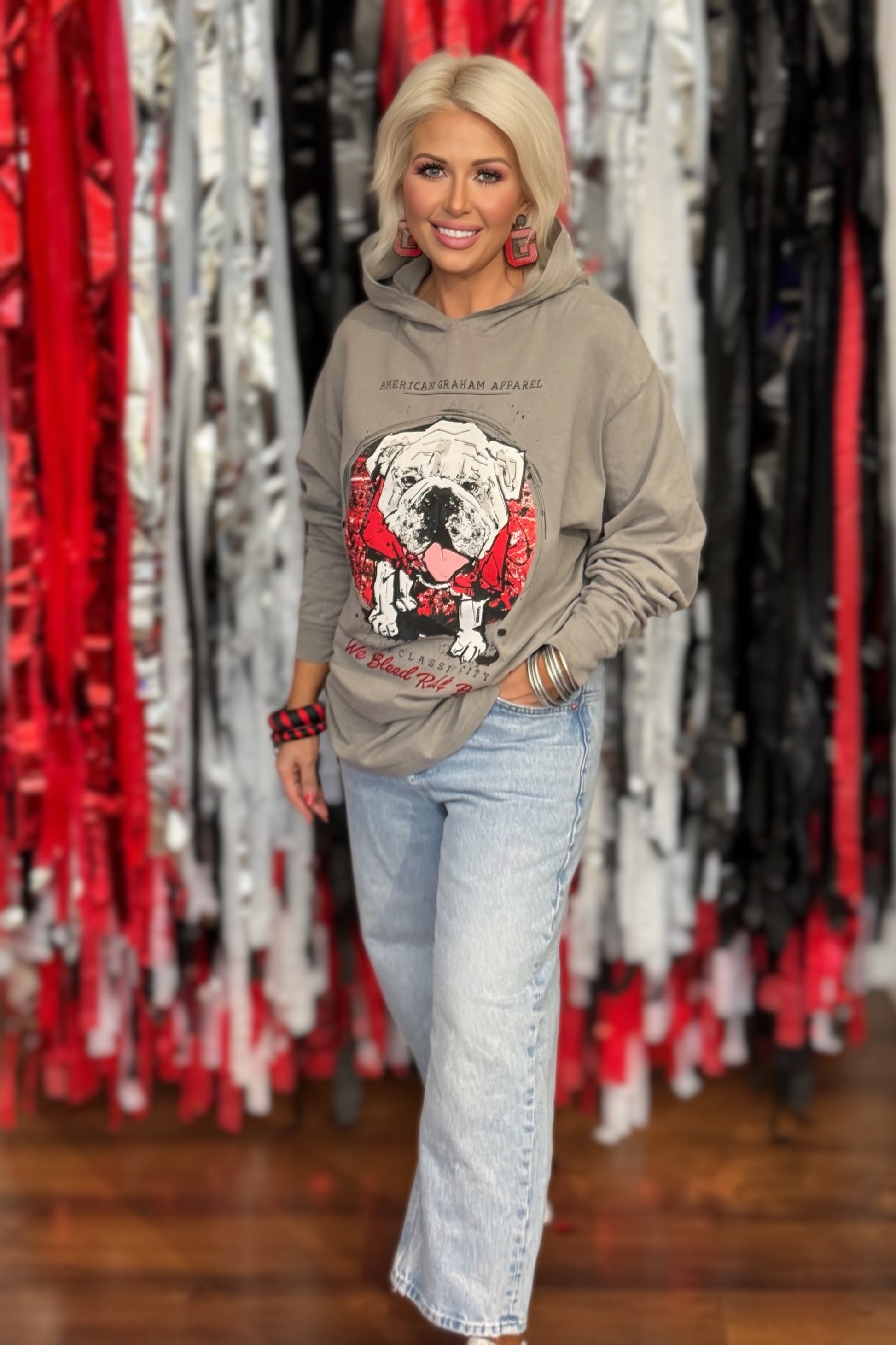 A person wearing a gray hooded long sleeve t-shirt with a large graphic print of a bulldog wearing a red bandana, with the text 'AMERICAN GRAHAM APPAREL' and 'The Classic City We Blood Red & Black' on the front.