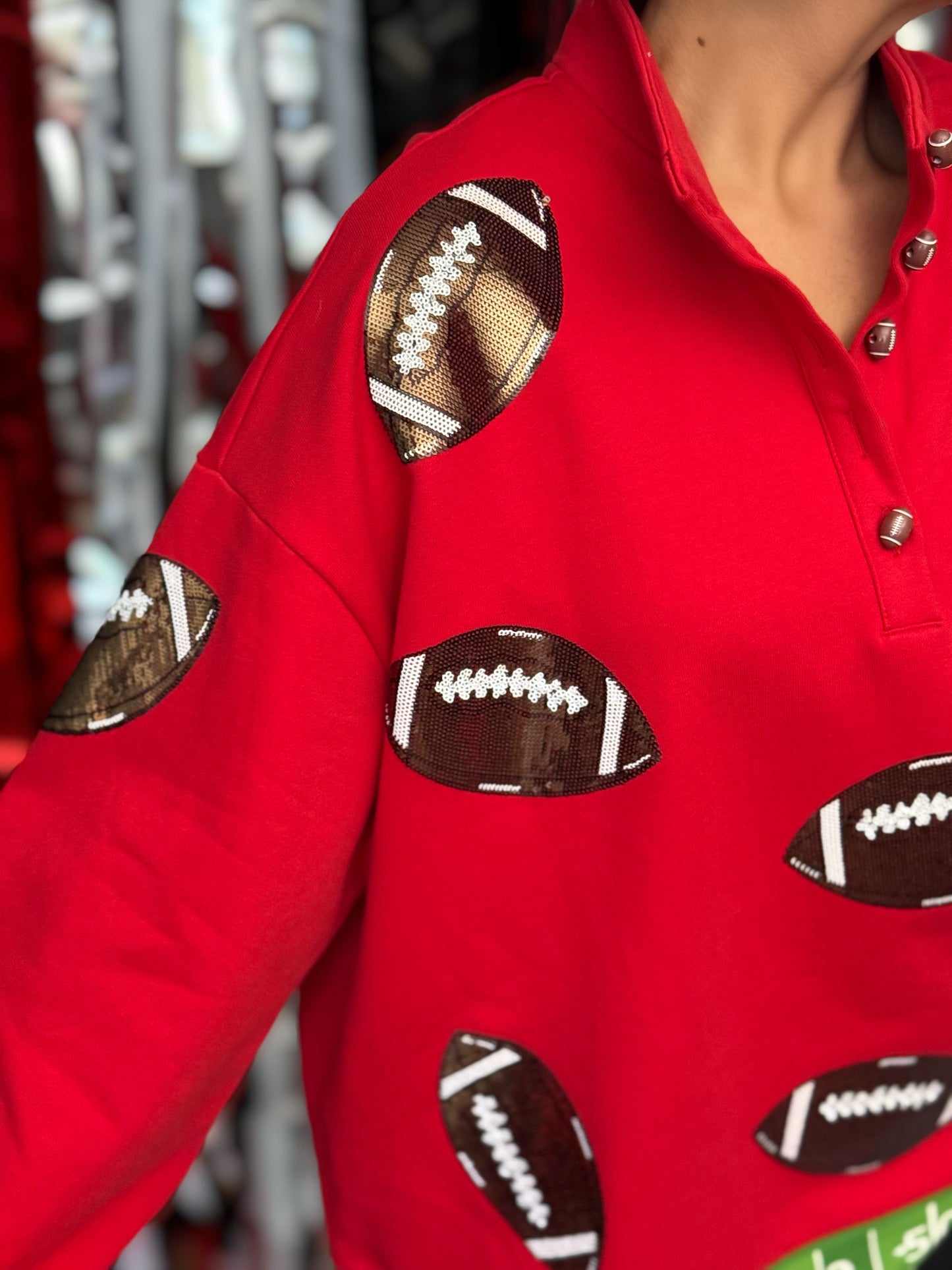 A close-up of a person wearing a bright red long-sleeve top with football-shaped appliques in brown, white, and black across the chest and sleeves.