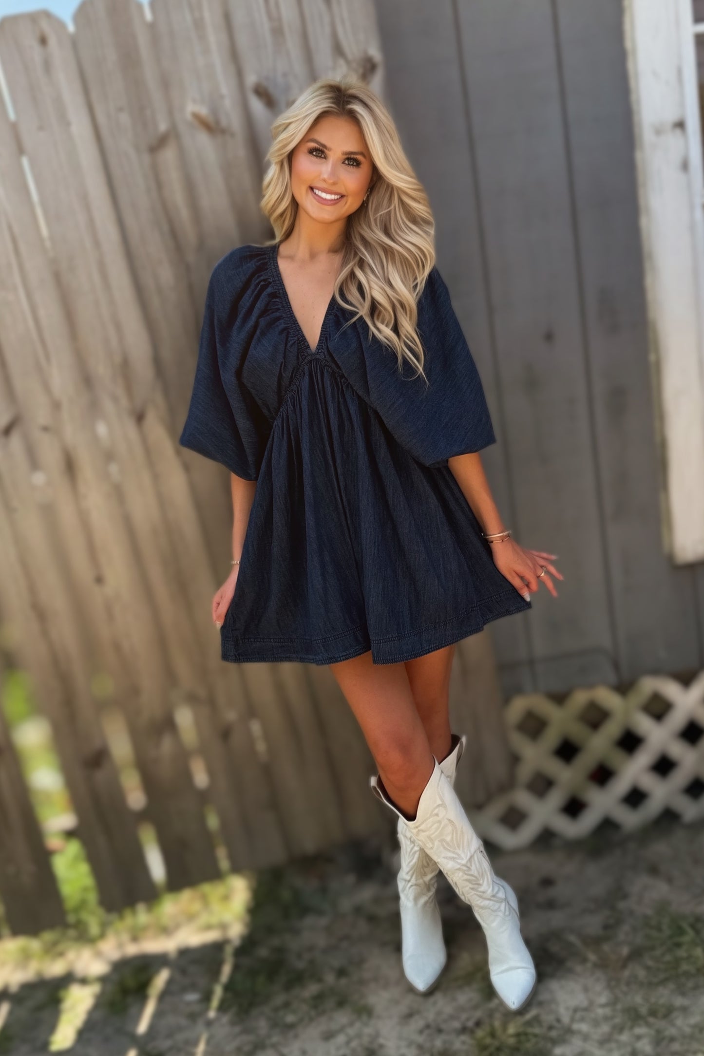 Woman wearing a dark wash denim mini dress with a deep V-neckline, three-quarter puff sleeves and a flared skirt.