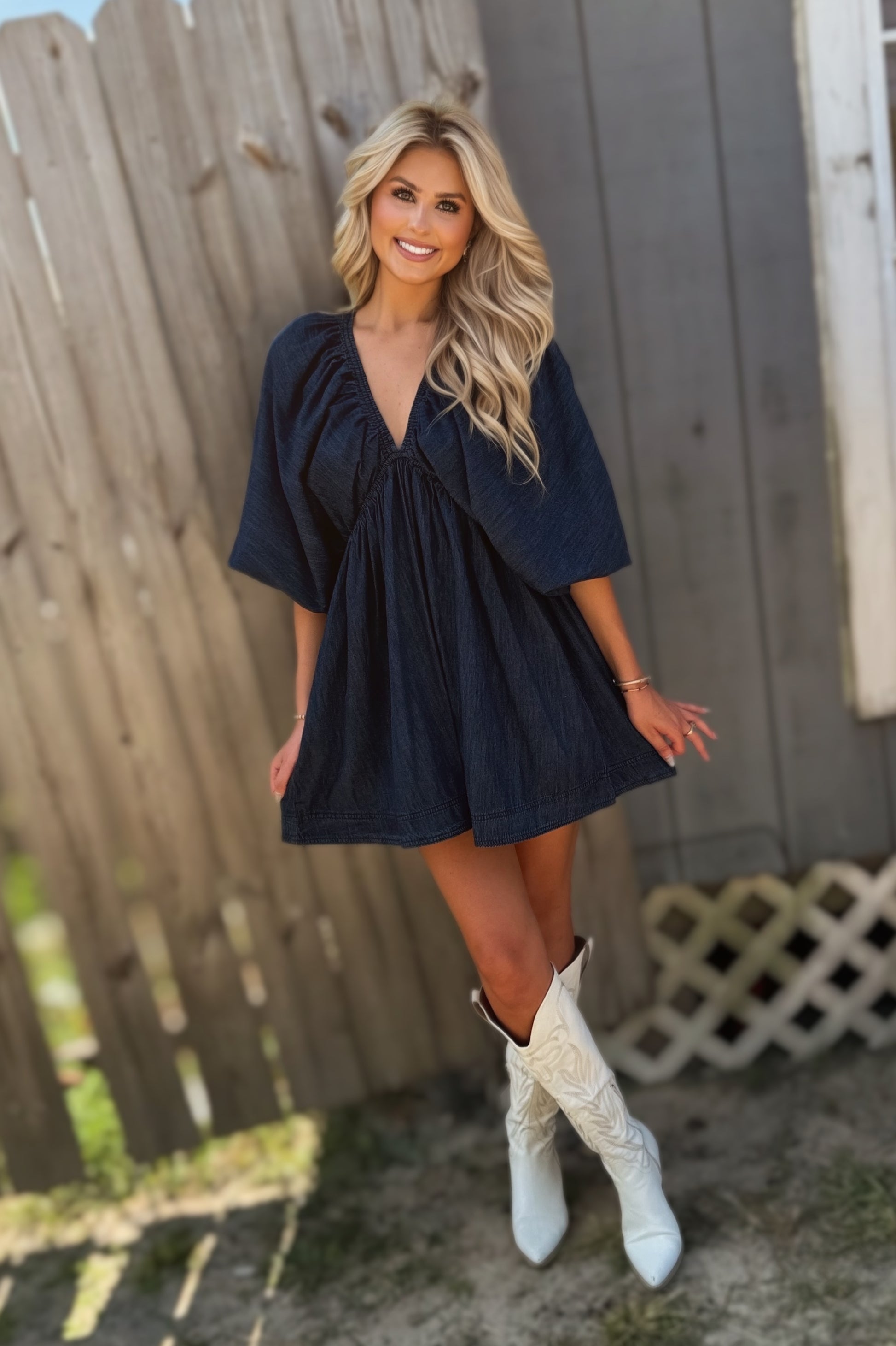 Woman wearing a dark wash denim mini dress with a deep V-neckline, three-quarter puff sleeves and a flared skirt.