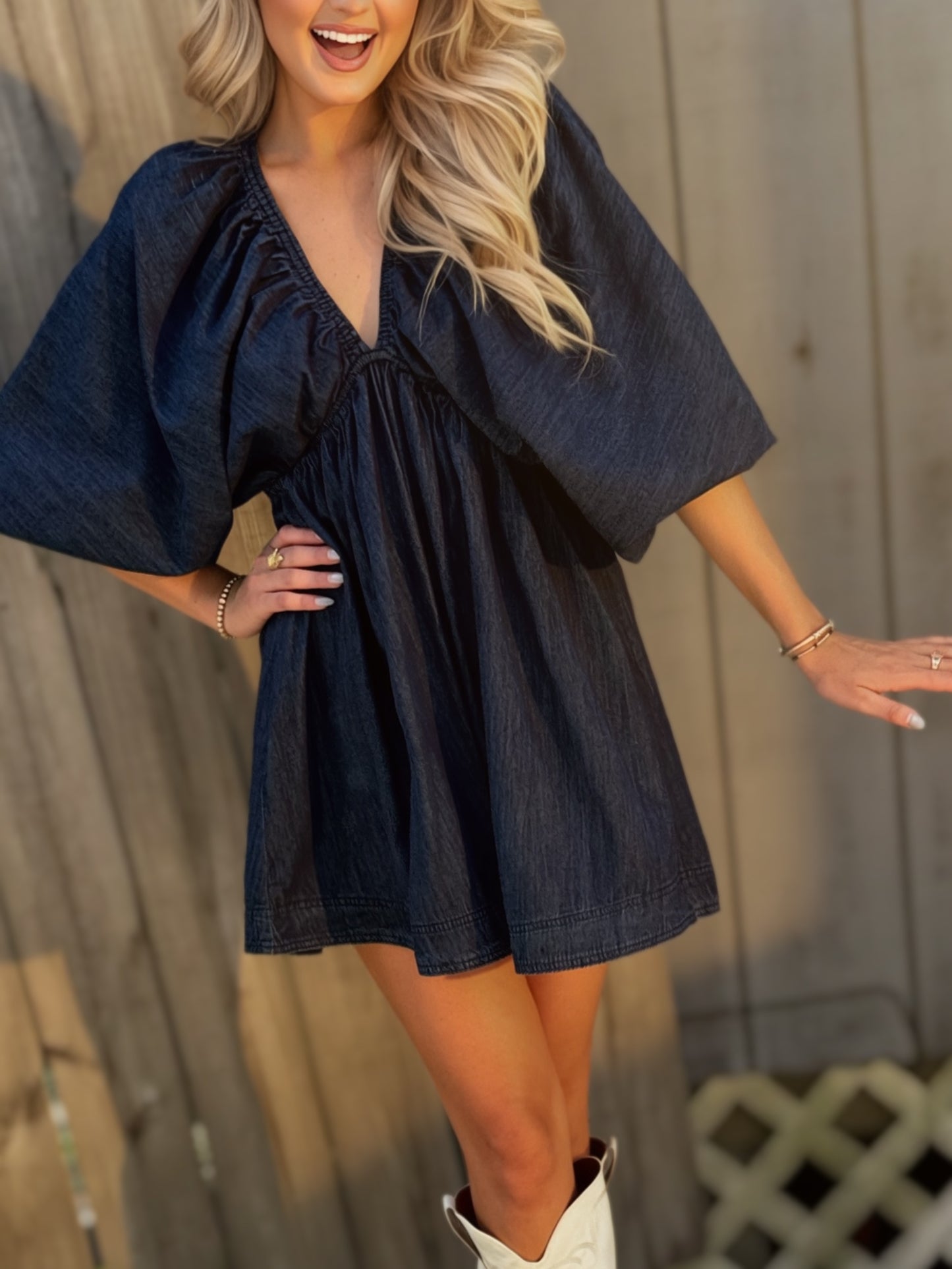 Woman wearing a dark wash denim mini dress with a deep V-neckline, three-quarter puff sleeves and a flared skirt.