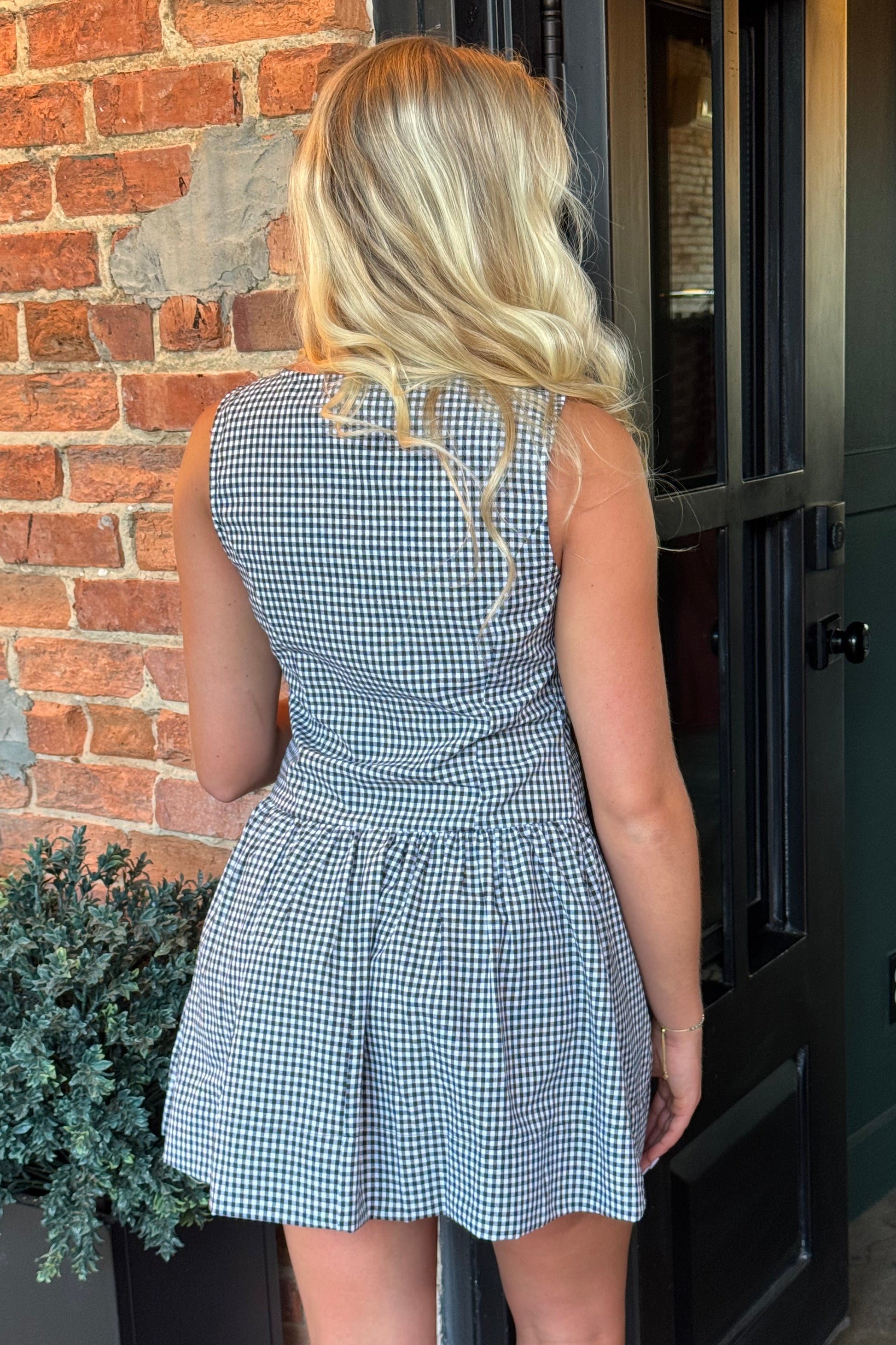 Woman wearing the Sienna black and white gingham sleeveless mini dress with a button-front bodice and gathered drop-waist skirt
