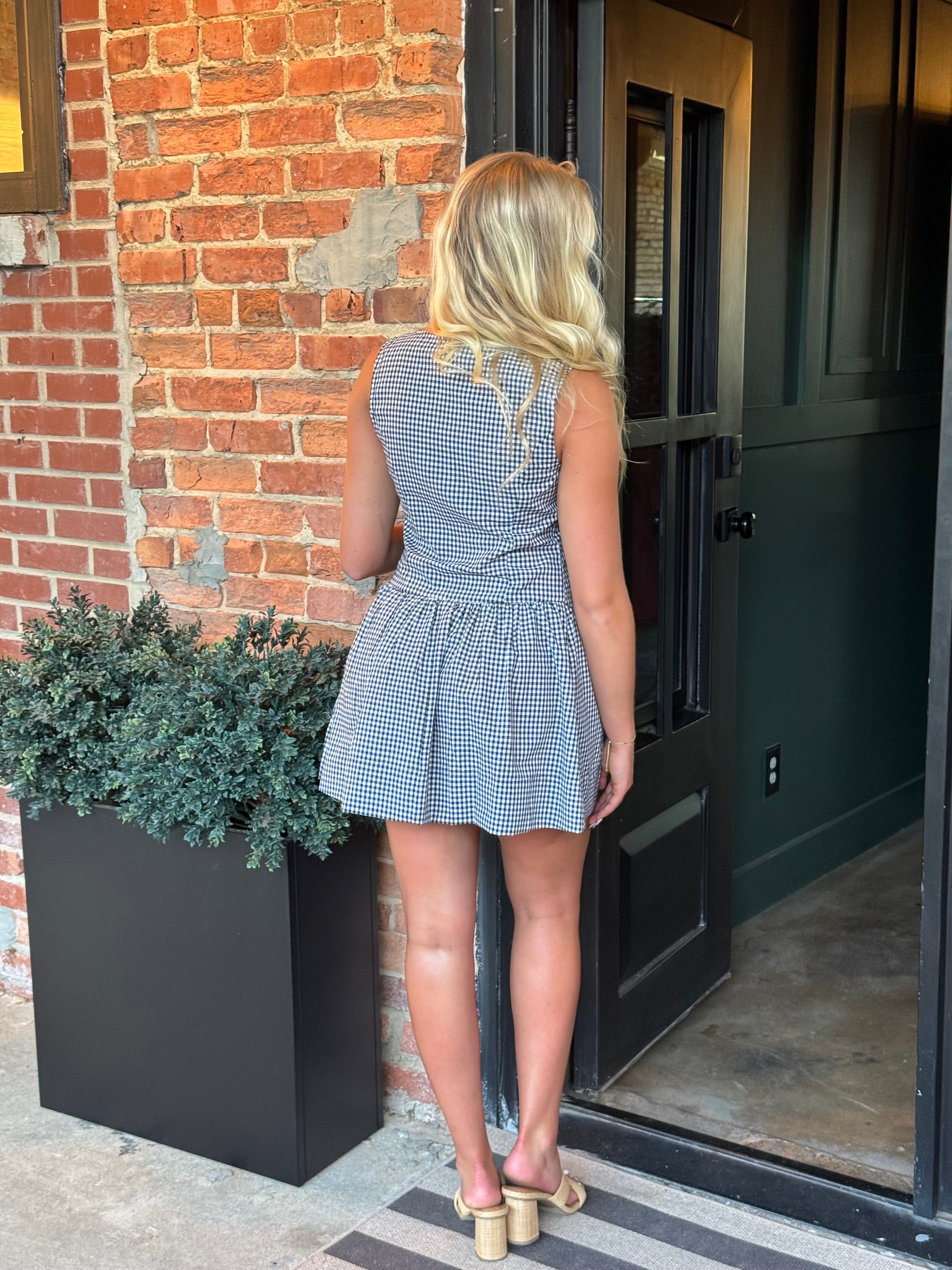 Woman wearing the Sienna black and white gingham sleeveless mini dress with a button-front bodice and gathered drop-waist skirt