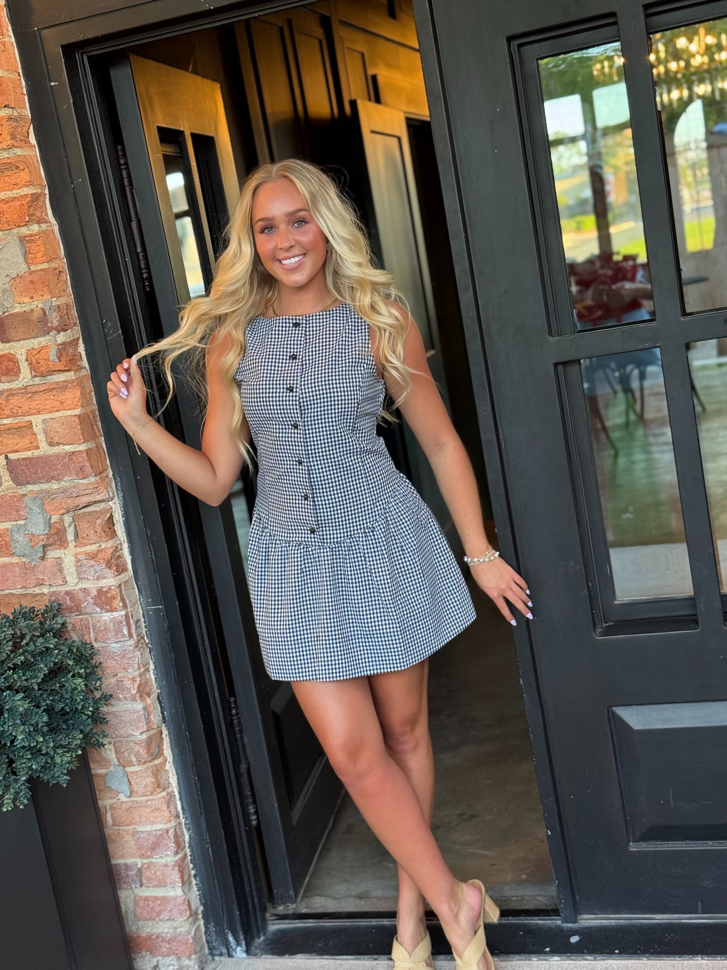 Woman wearing the Sienna black and white gingham sleeveless mini dress with a button-front bodice and gathered drop-waist skirt