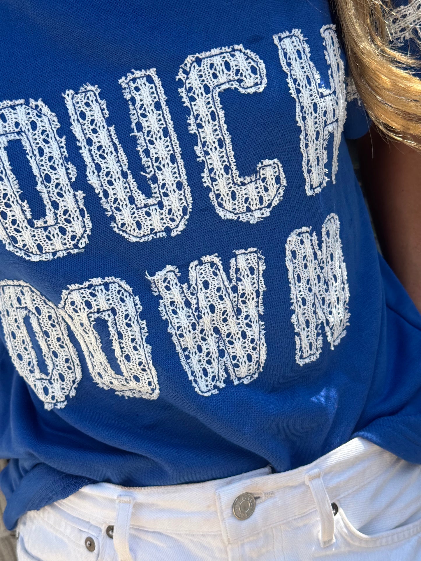 Woman wearing a royal blue Touchdown game day top with white lace lettering and lace-trimmed bubble sleeves.