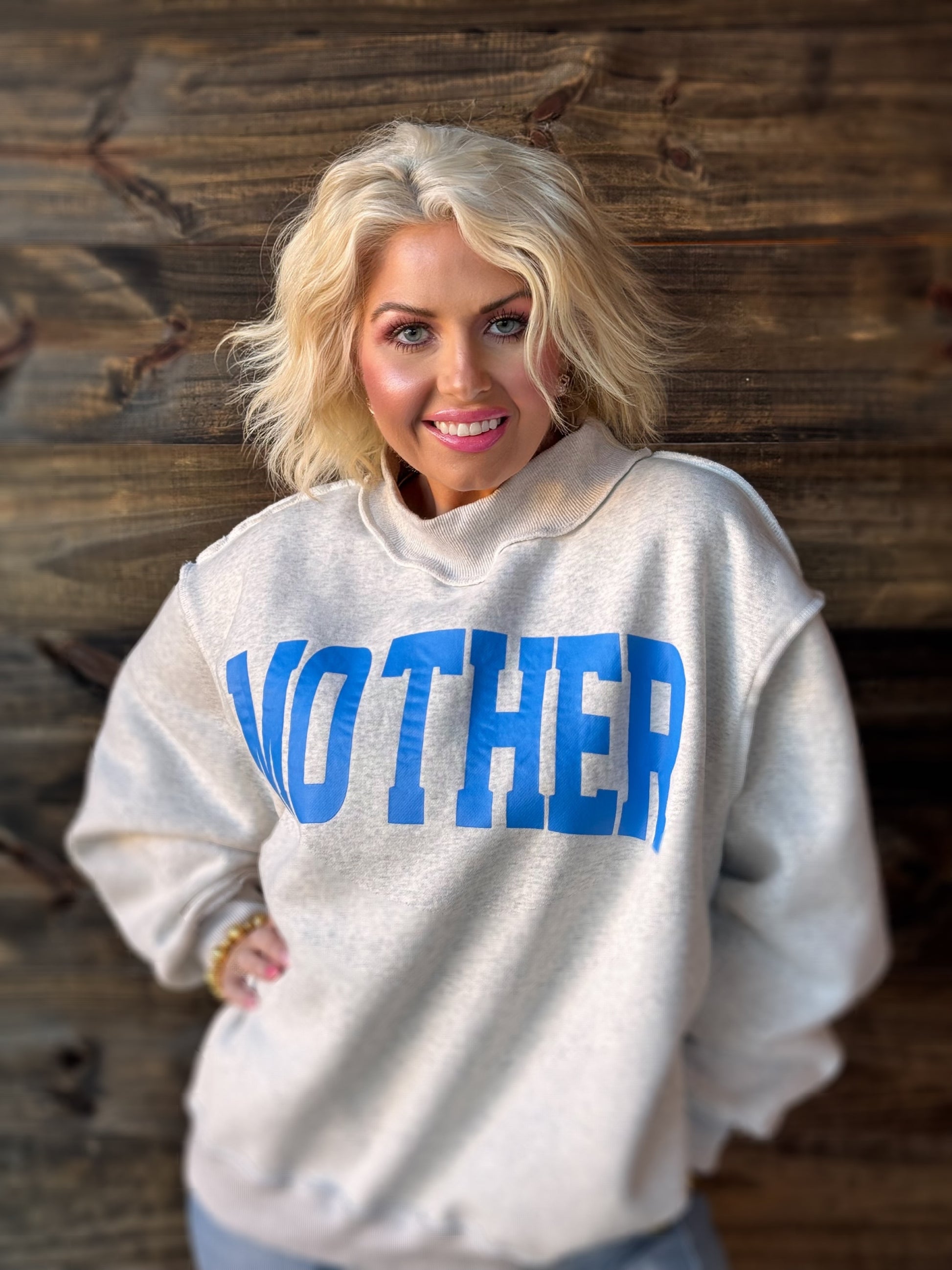 Woman wearing a sweatshirt with 'MOTHER' printed on it against a wooden background
