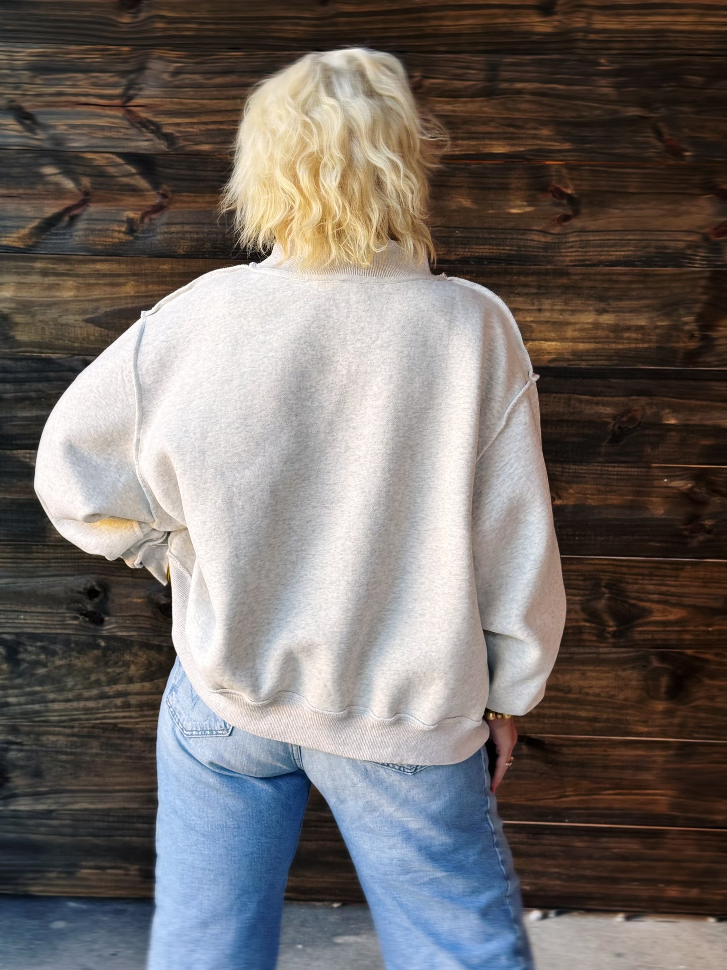 Person wearing a beige sweater and blue jeans against a wooden wall