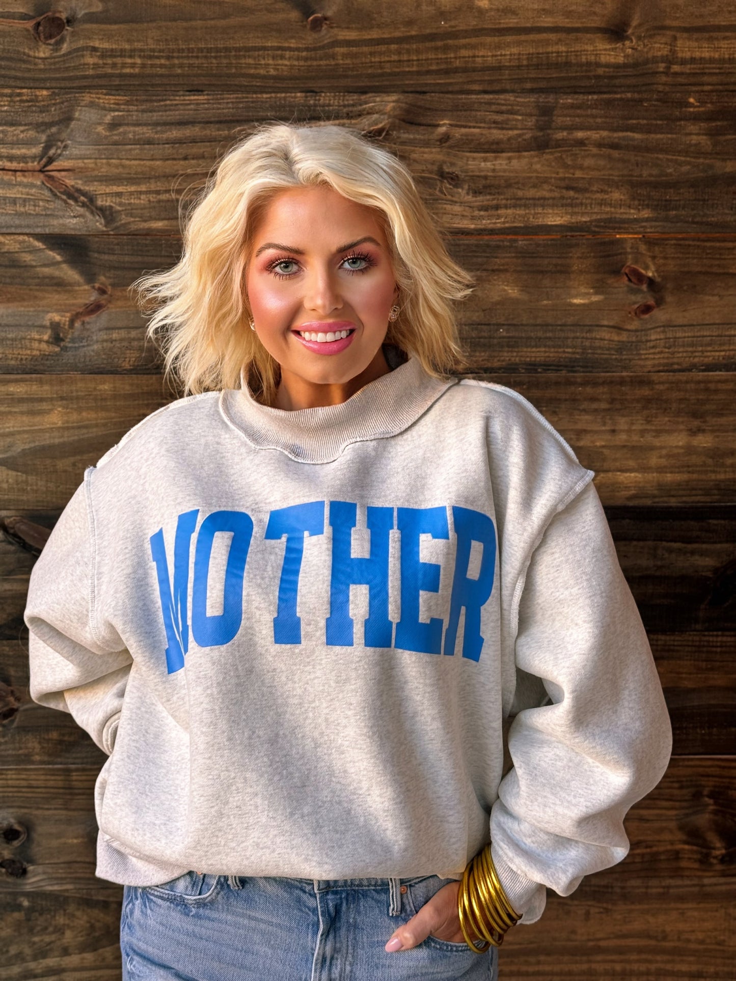 Woman wearing a gray sweatshirt with 'MOther' printed in blue letters against a wooden background