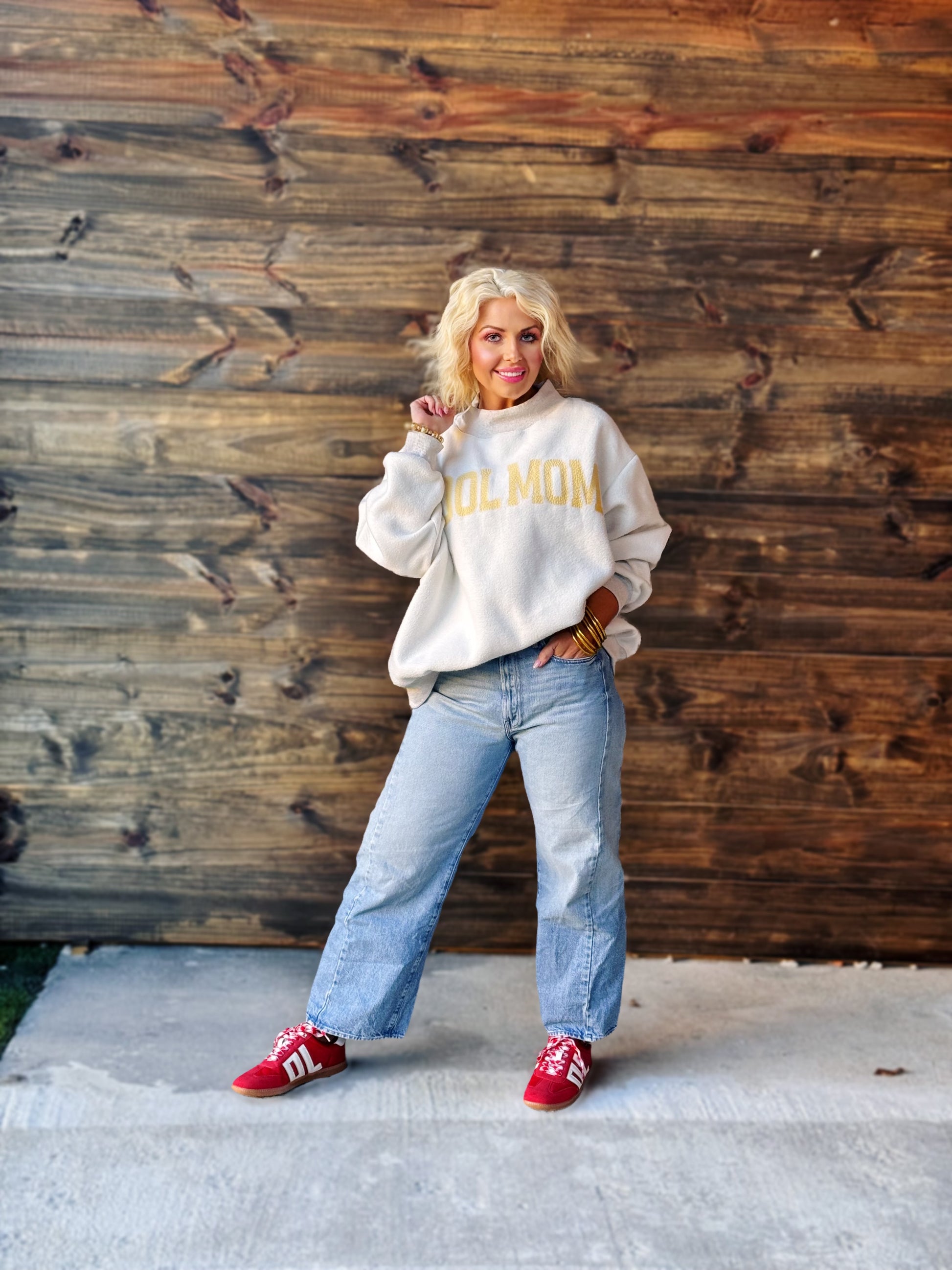 Person wearing a sweatshirt with 'COOL MOM' text, standing against a wooden wall.