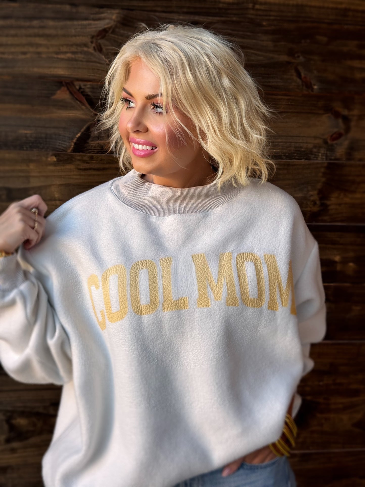 Woman wearing a white sweatshirt with 'COOL MOM' text against a wooden background