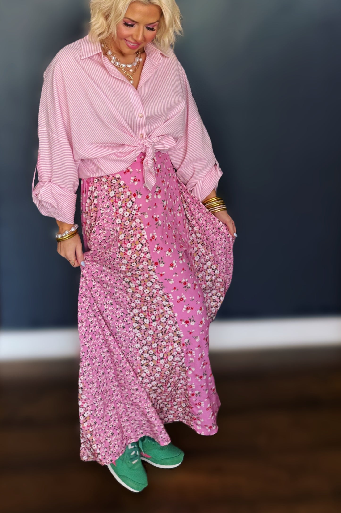 Woman wearing a pink outfit with a floral skirt and green shoes against a dark background