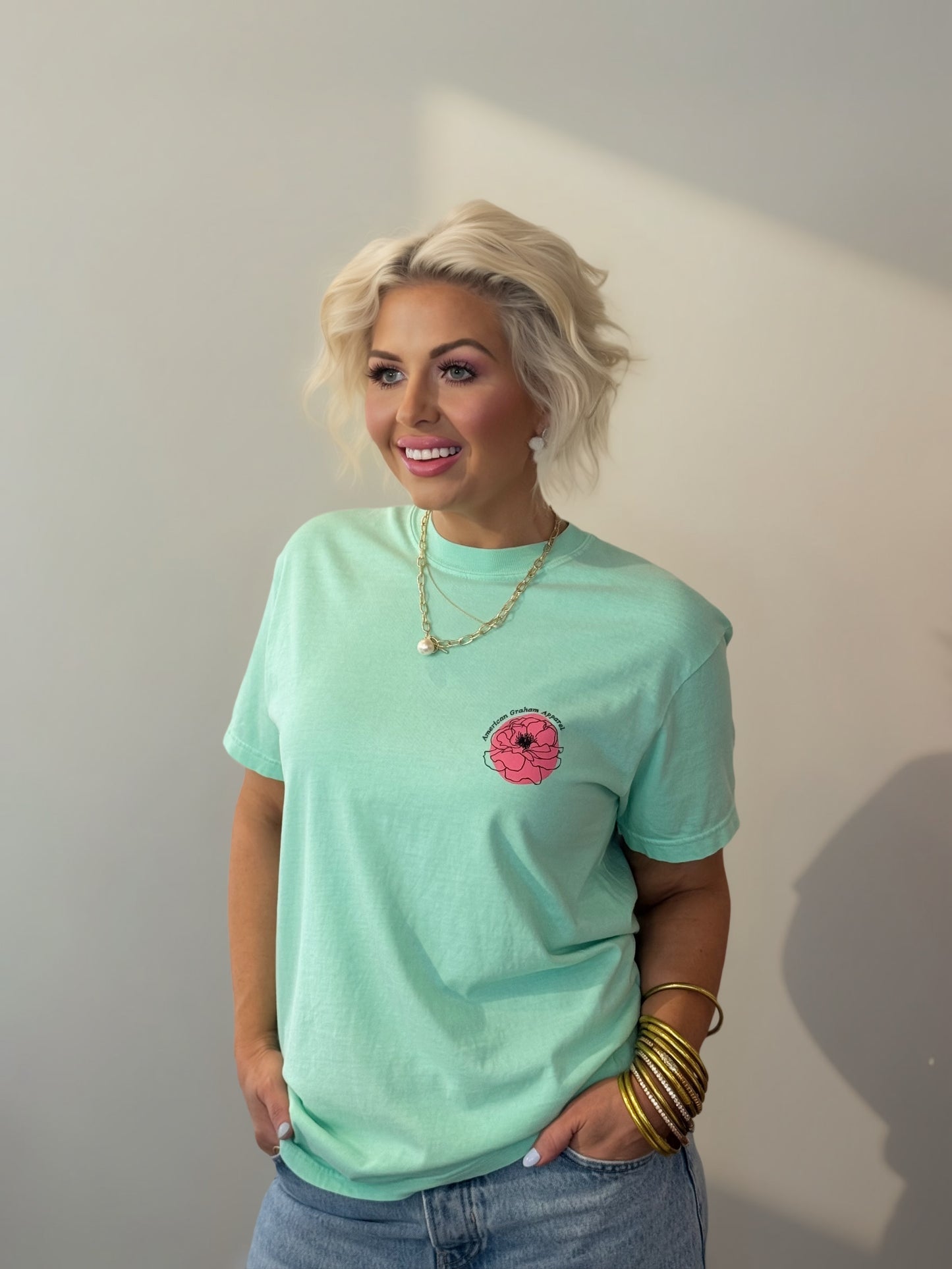 Woman wearing a light green t-shirt with a pink flower design against a plain background