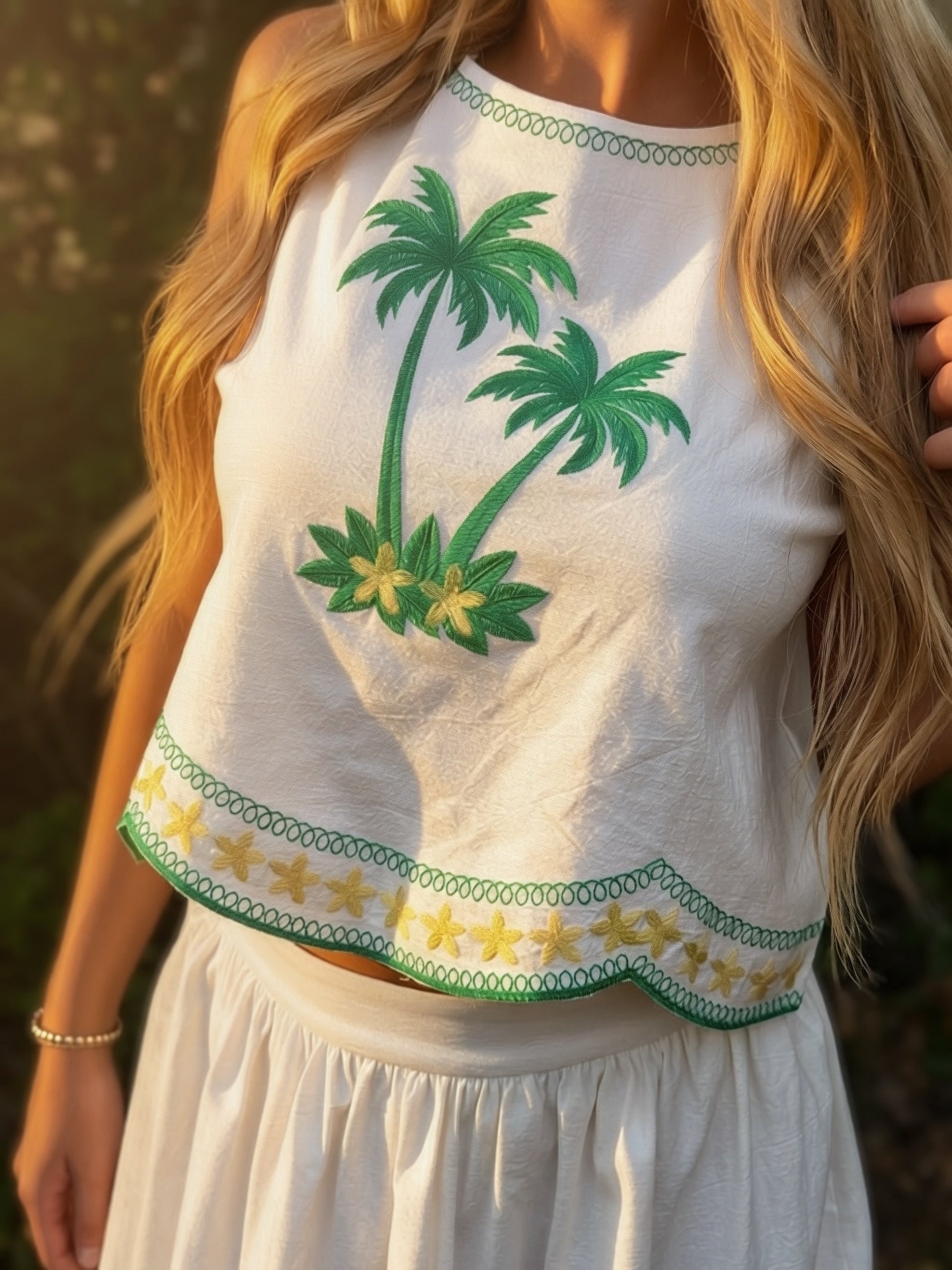 White sleeveless top with green palm tree designs worn by a person.